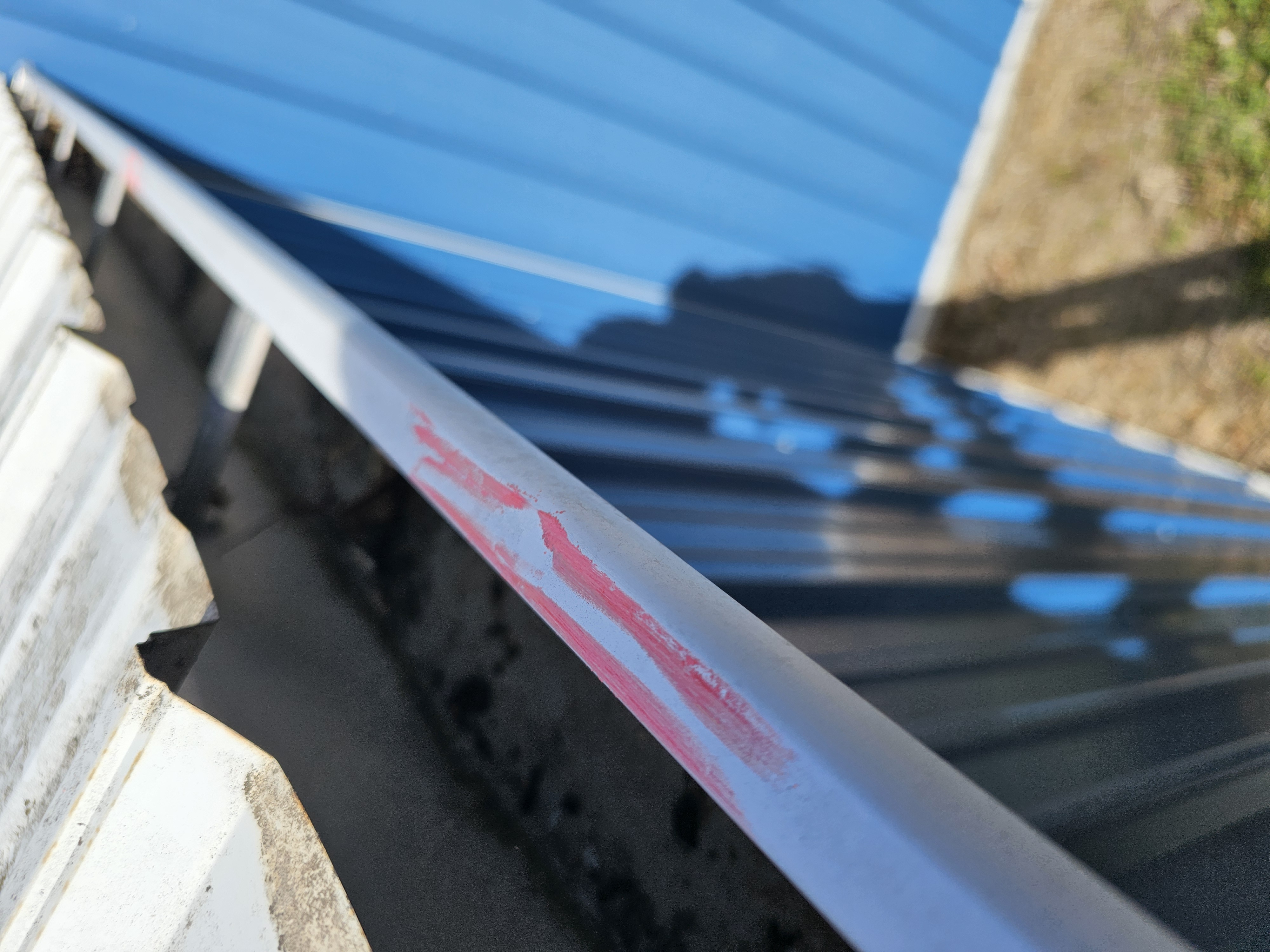 Close-up of a metal roof edge with a blue wall and gutter