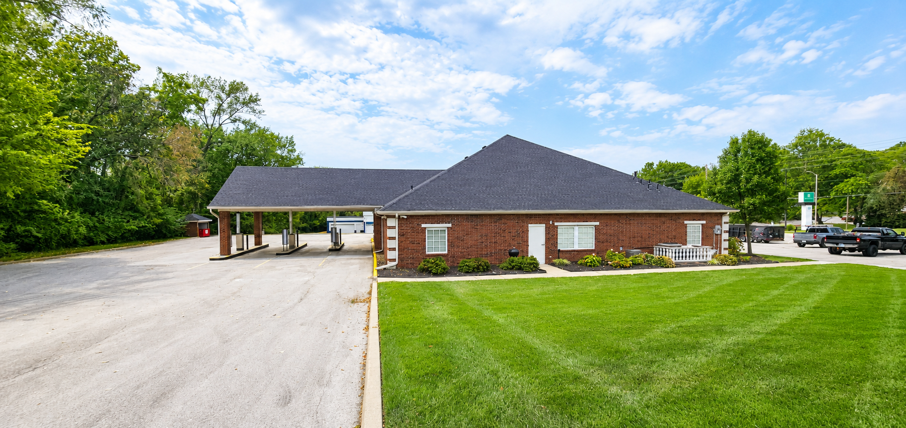 Brick building with a dark roof and a well-maintained lawn under a partly cloudy sky