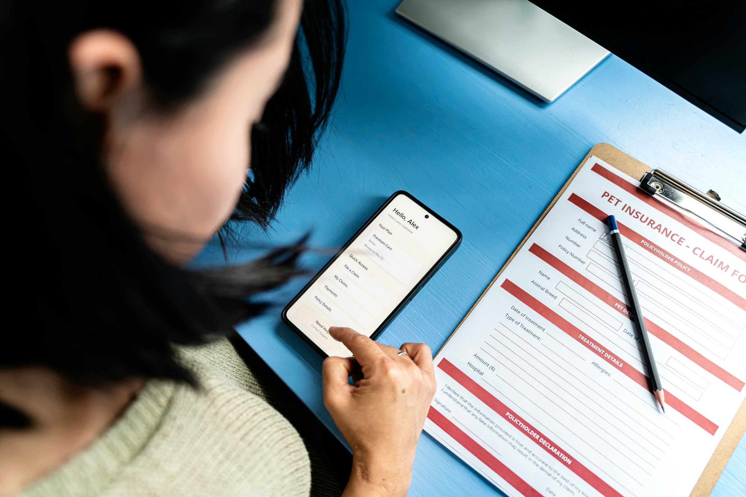 Person using a smartphone next to a pet insurance claim form on a clipboard