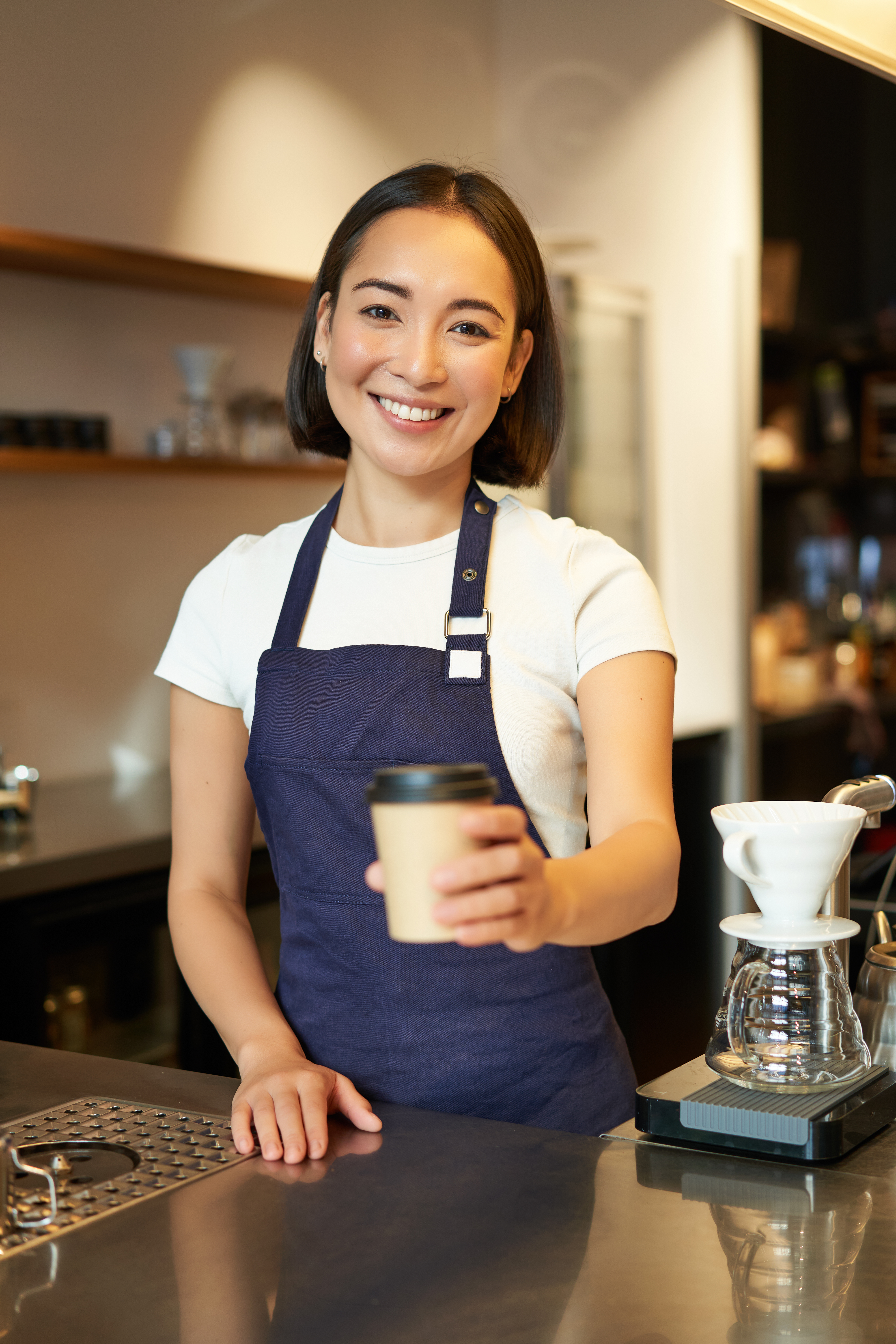 Smiling barista offering a cup of coffee at a cafe counter