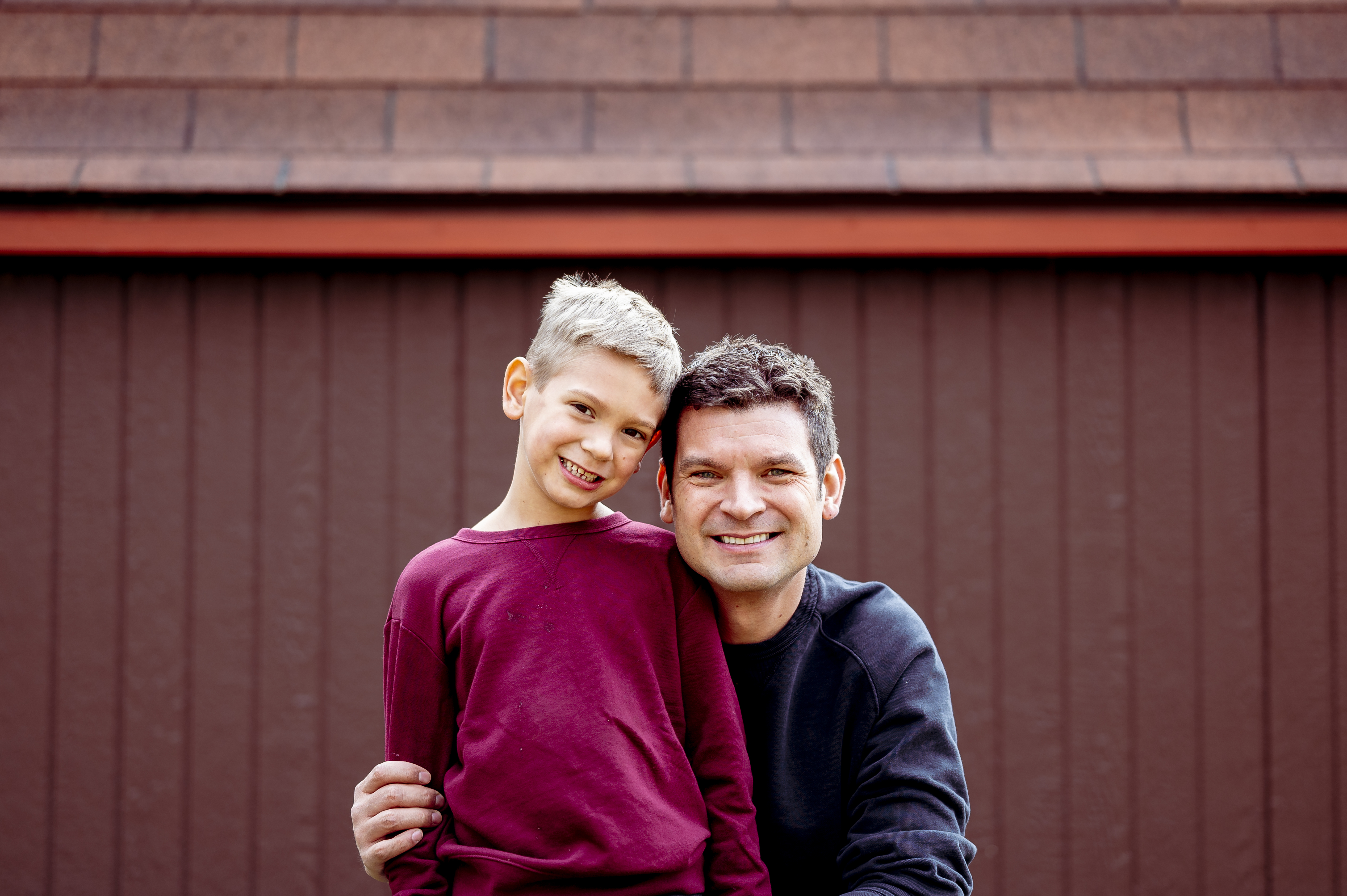 Smiling father and son standing in front of a brown building