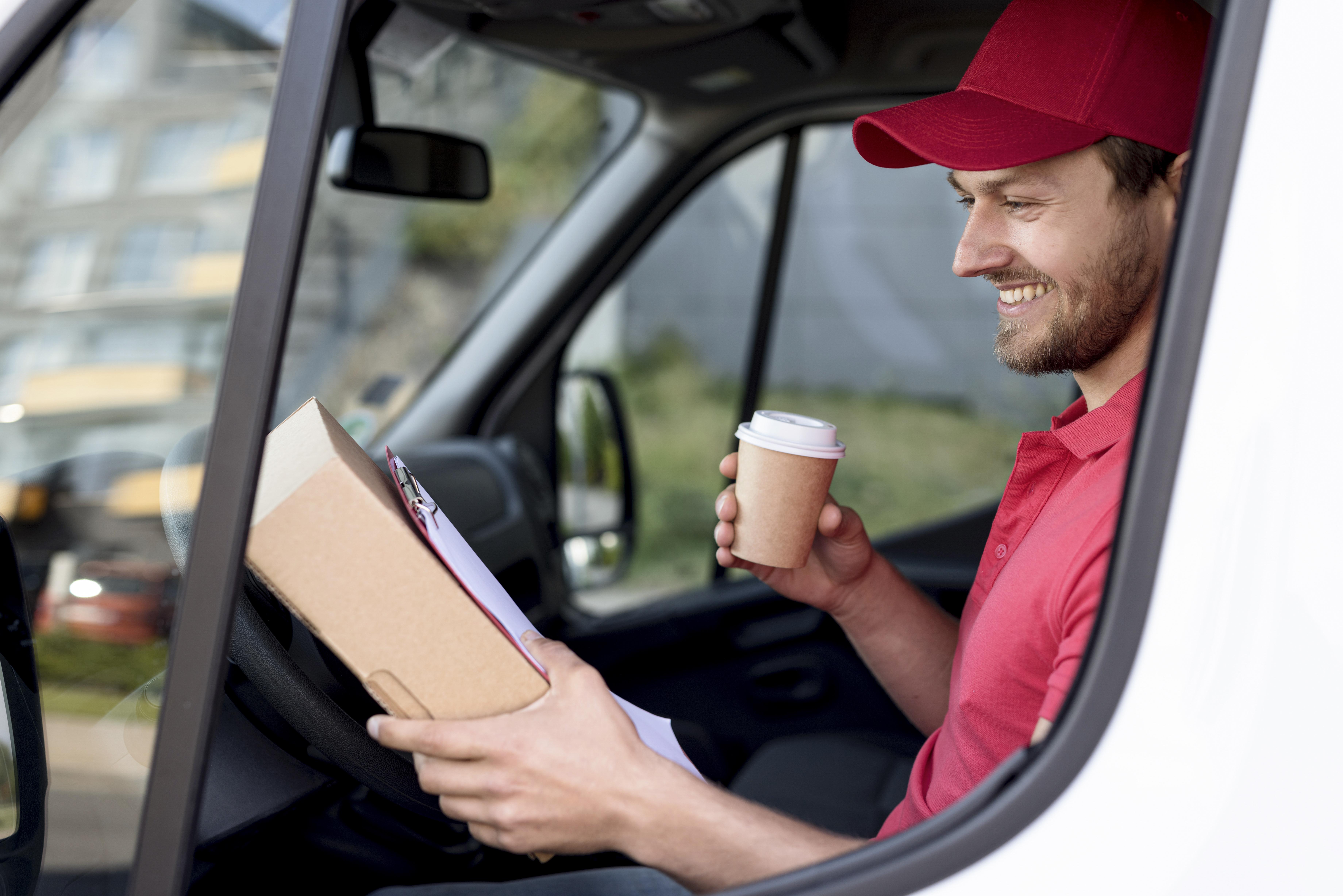 Delivery driver in red uniform holding a package and coffee inside a van