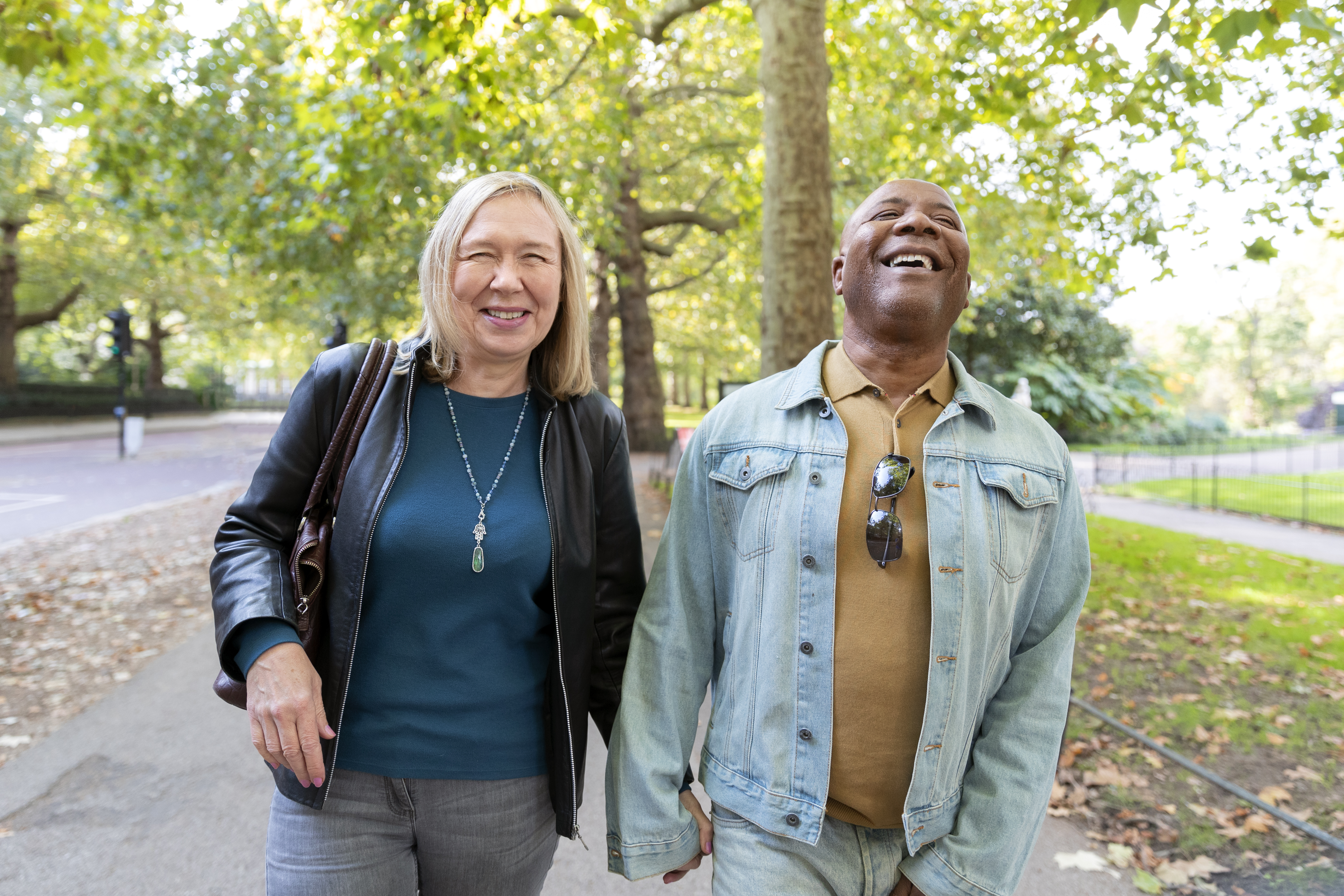 Two people walking and laughing in a park with trees in the background