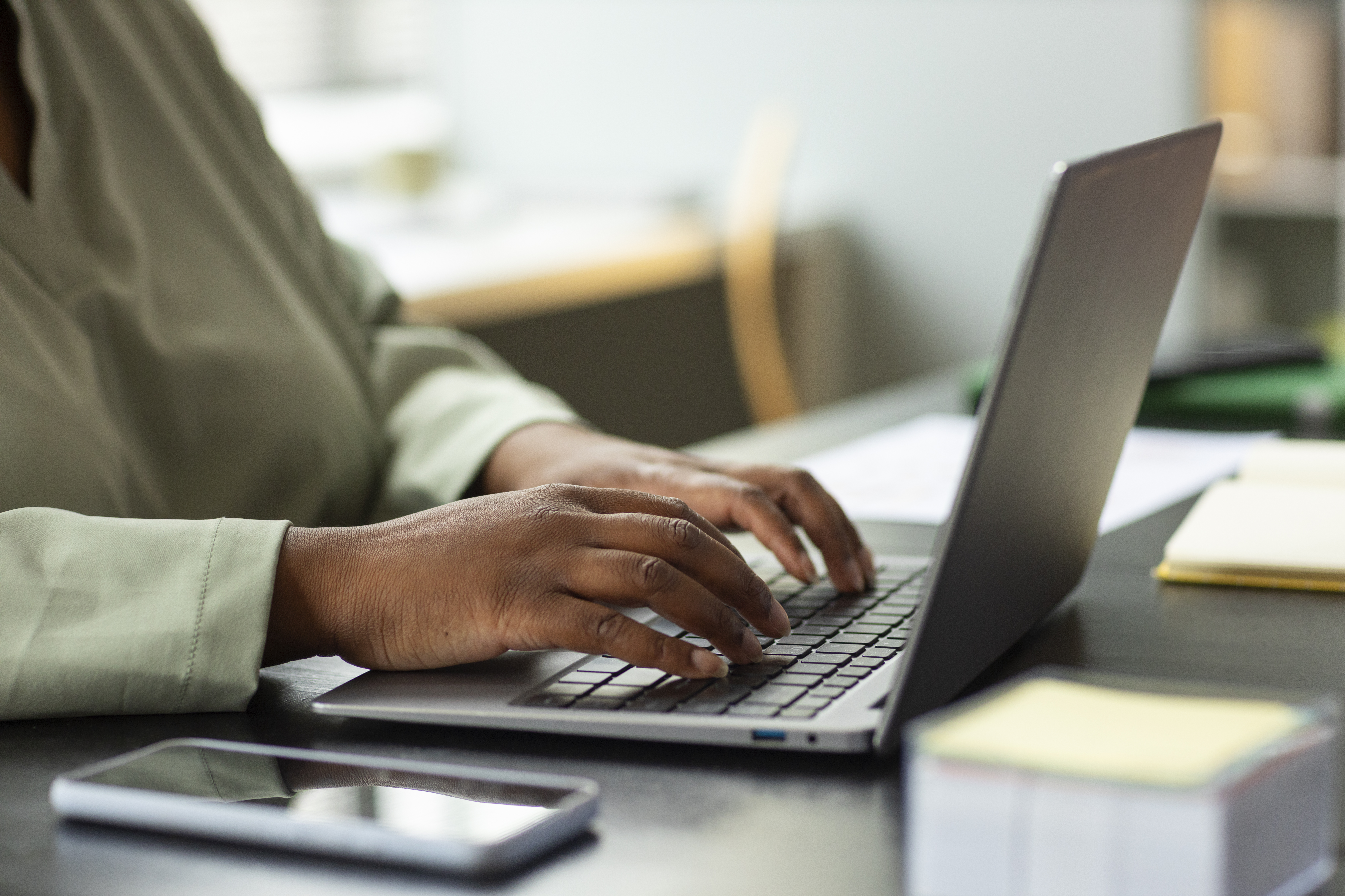 Person typing on a laptop at a desk with a smartphone nearby