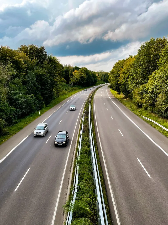 Cars driving on a divided highway surrounded by trees under a cloudy sky