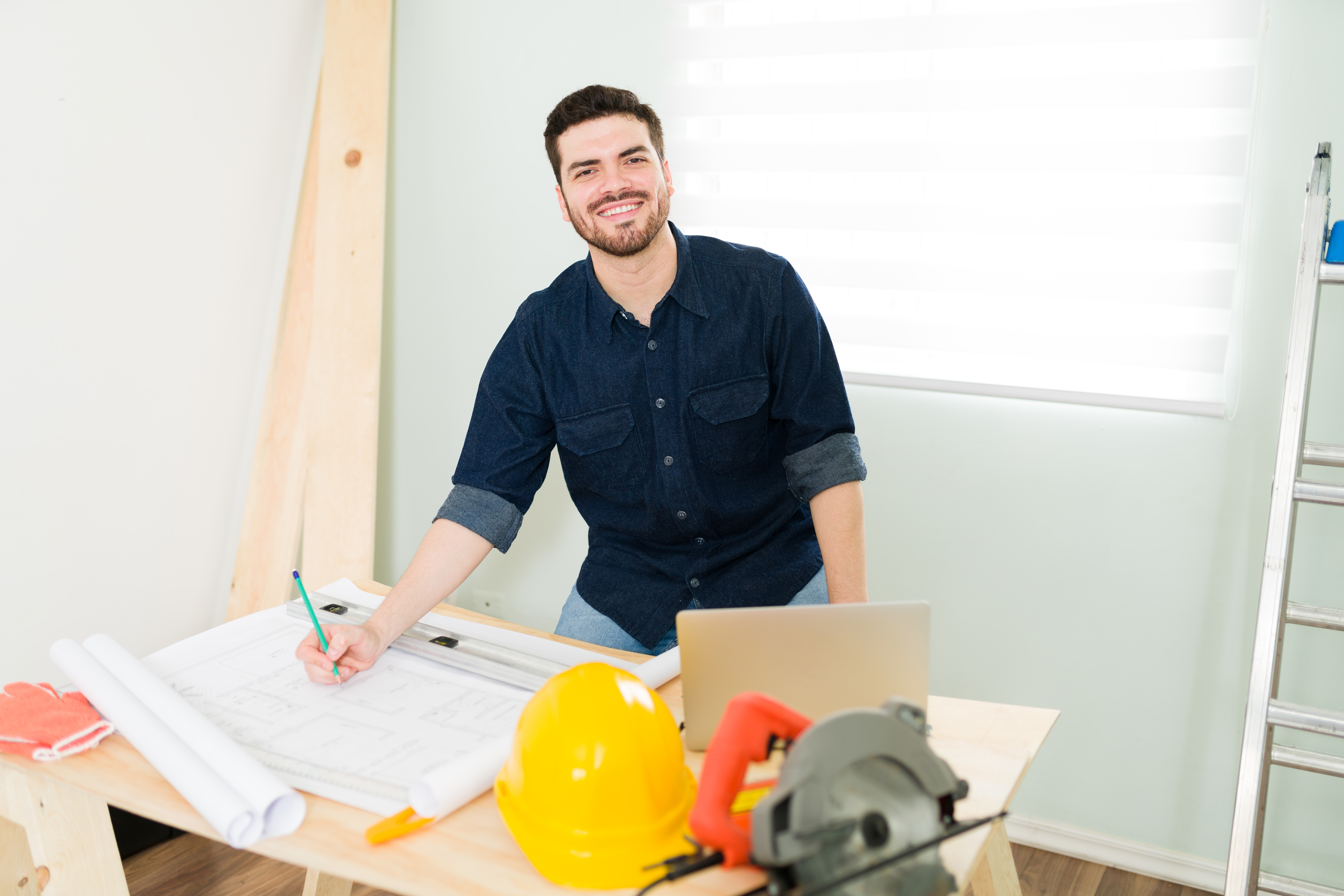 Smiling man working on architectural plans at a desk with construction tools.