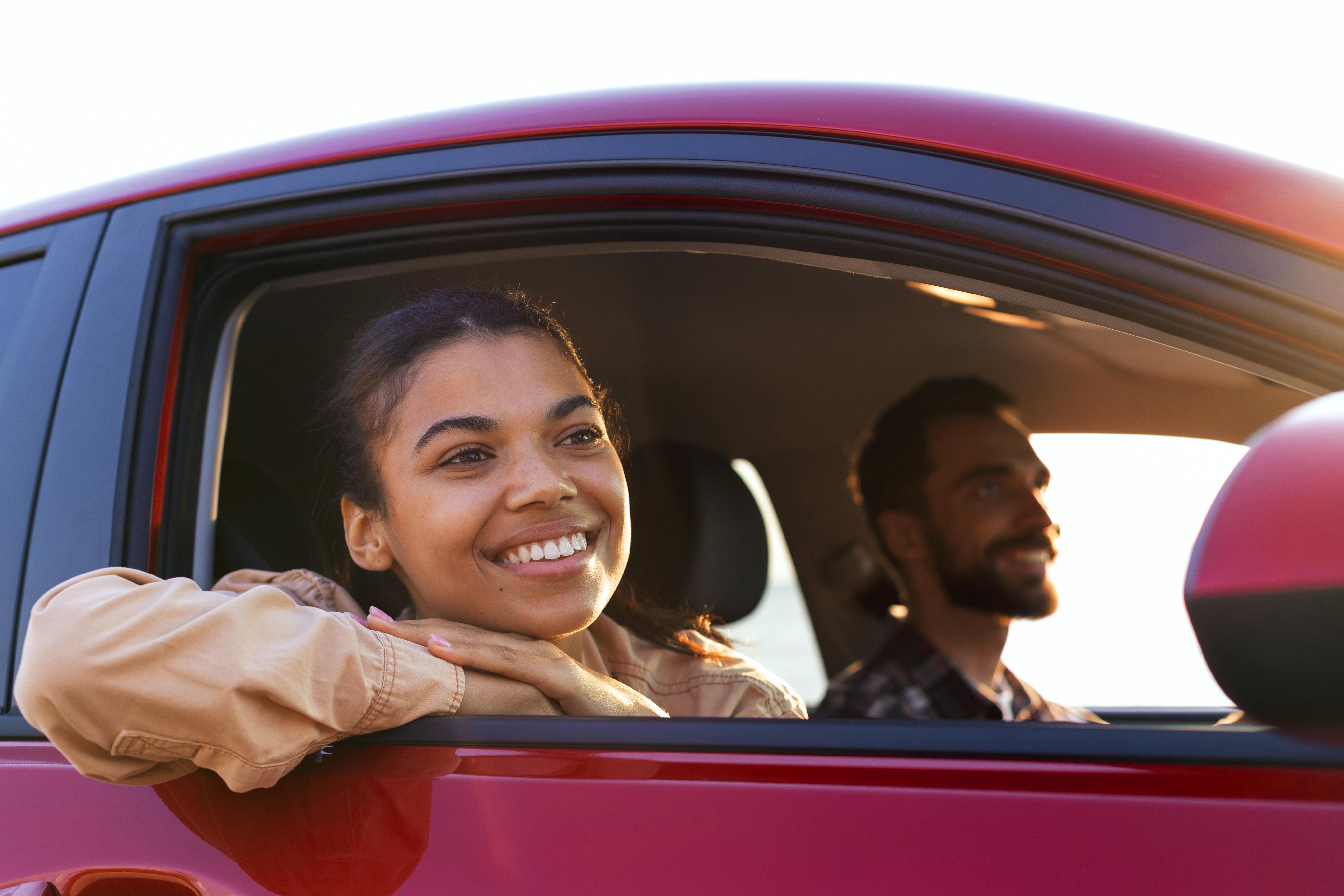 Smiling woman looking out of a red car window with a man driving