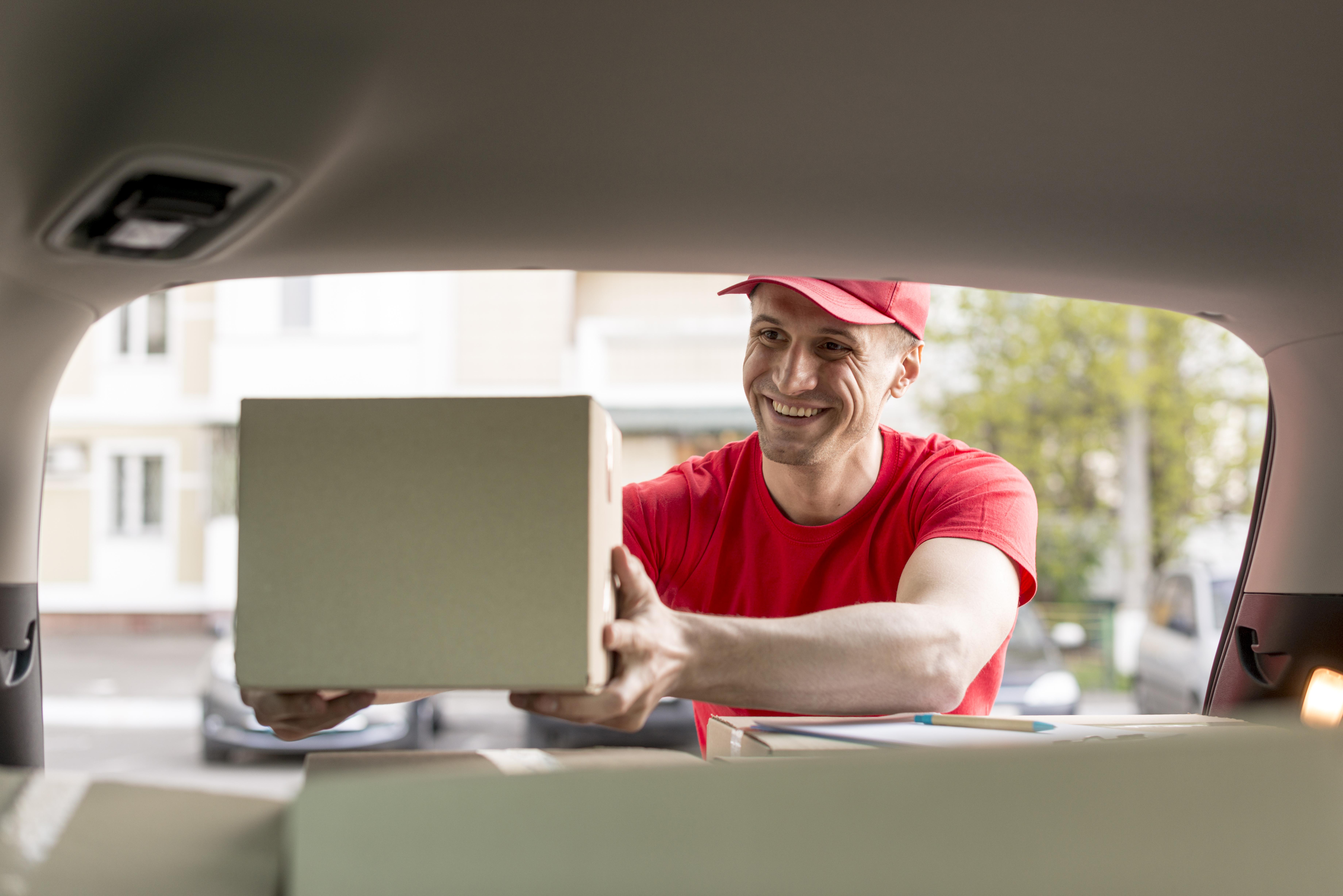 Delivery person in red uniform loading boxes into a vehicle.