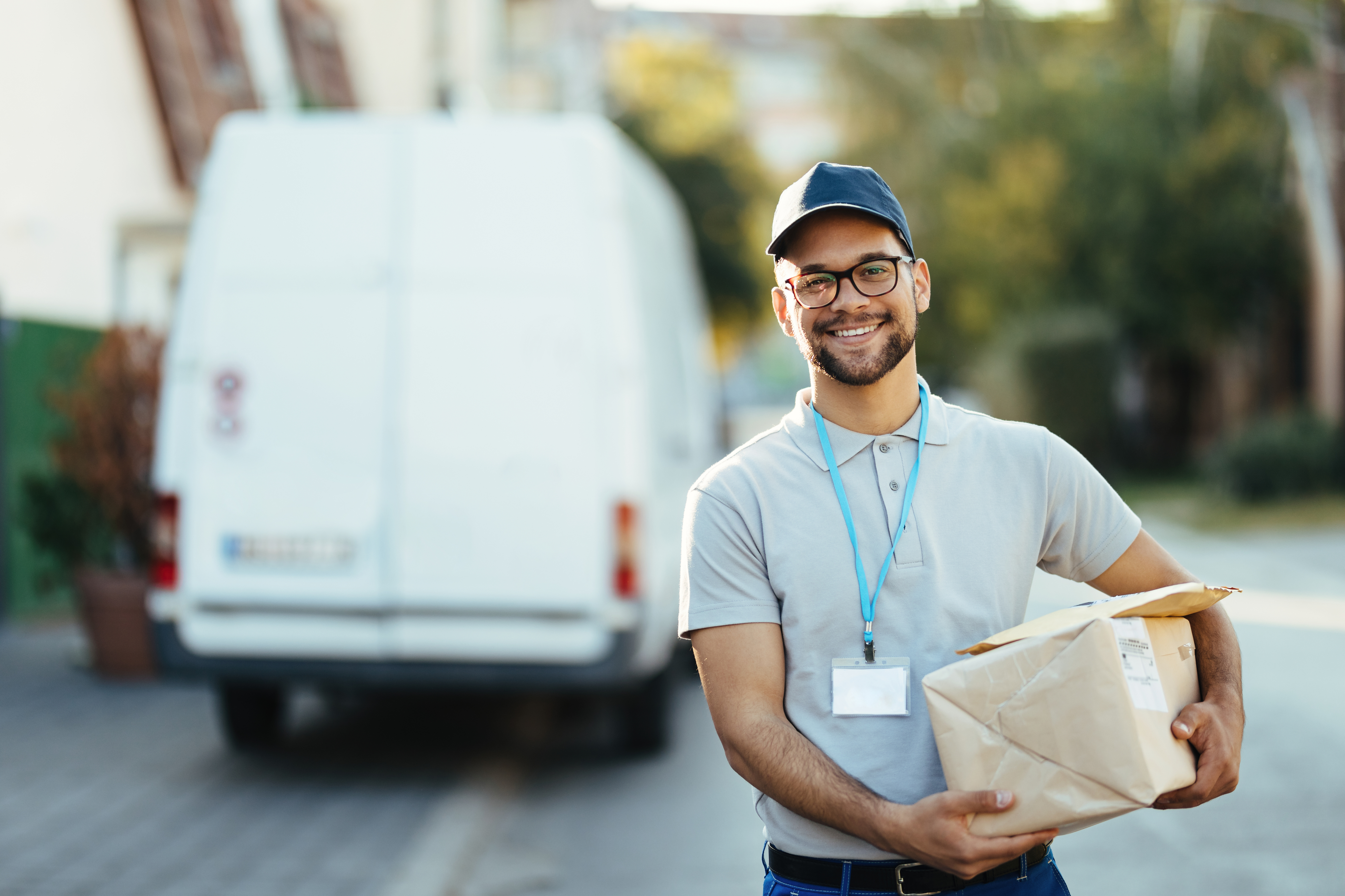 Delivery person holding a package in front of a van on a sunny day