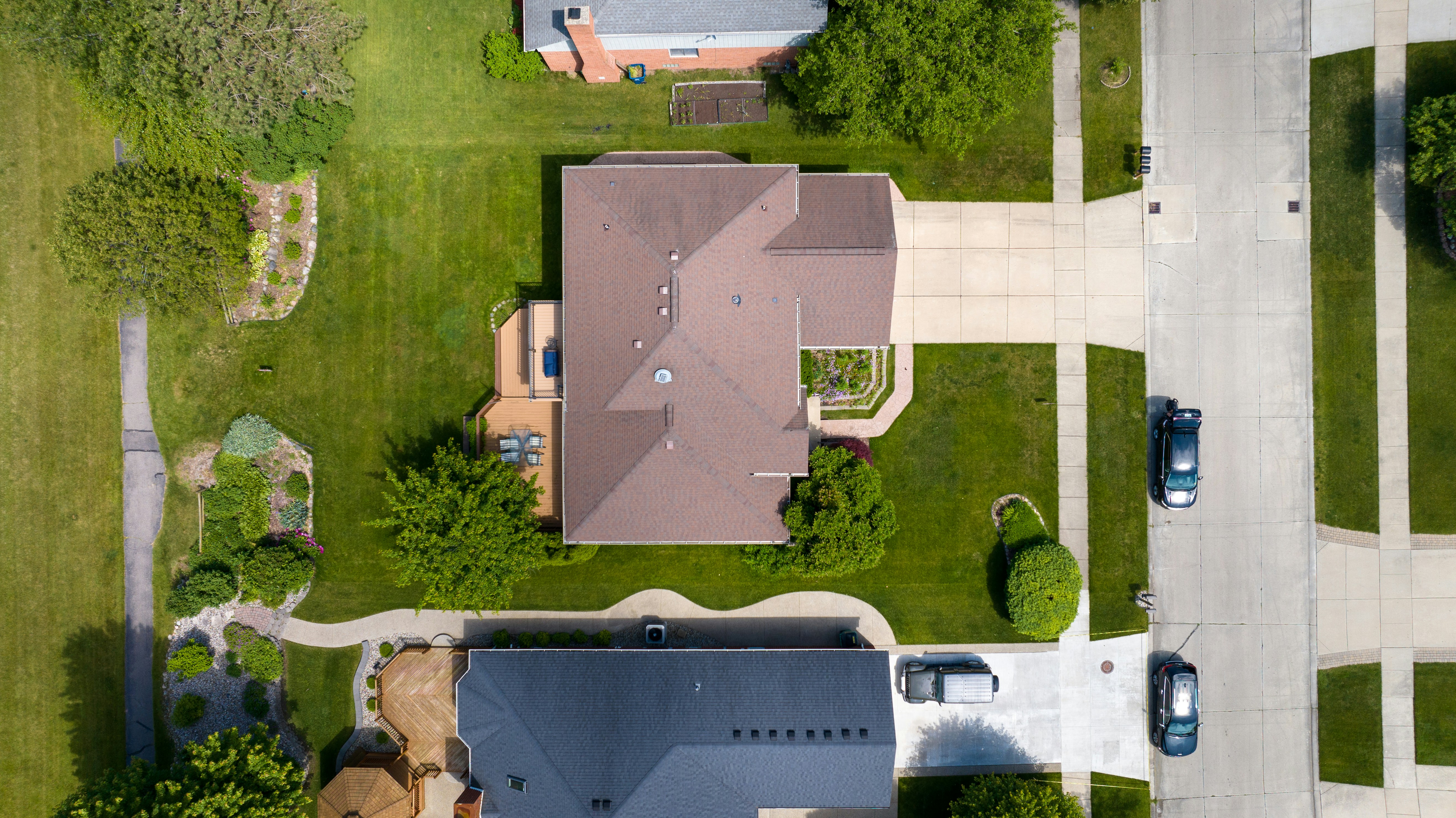 Gray shingle roof with a black vent near a brick wall and green trees in the background