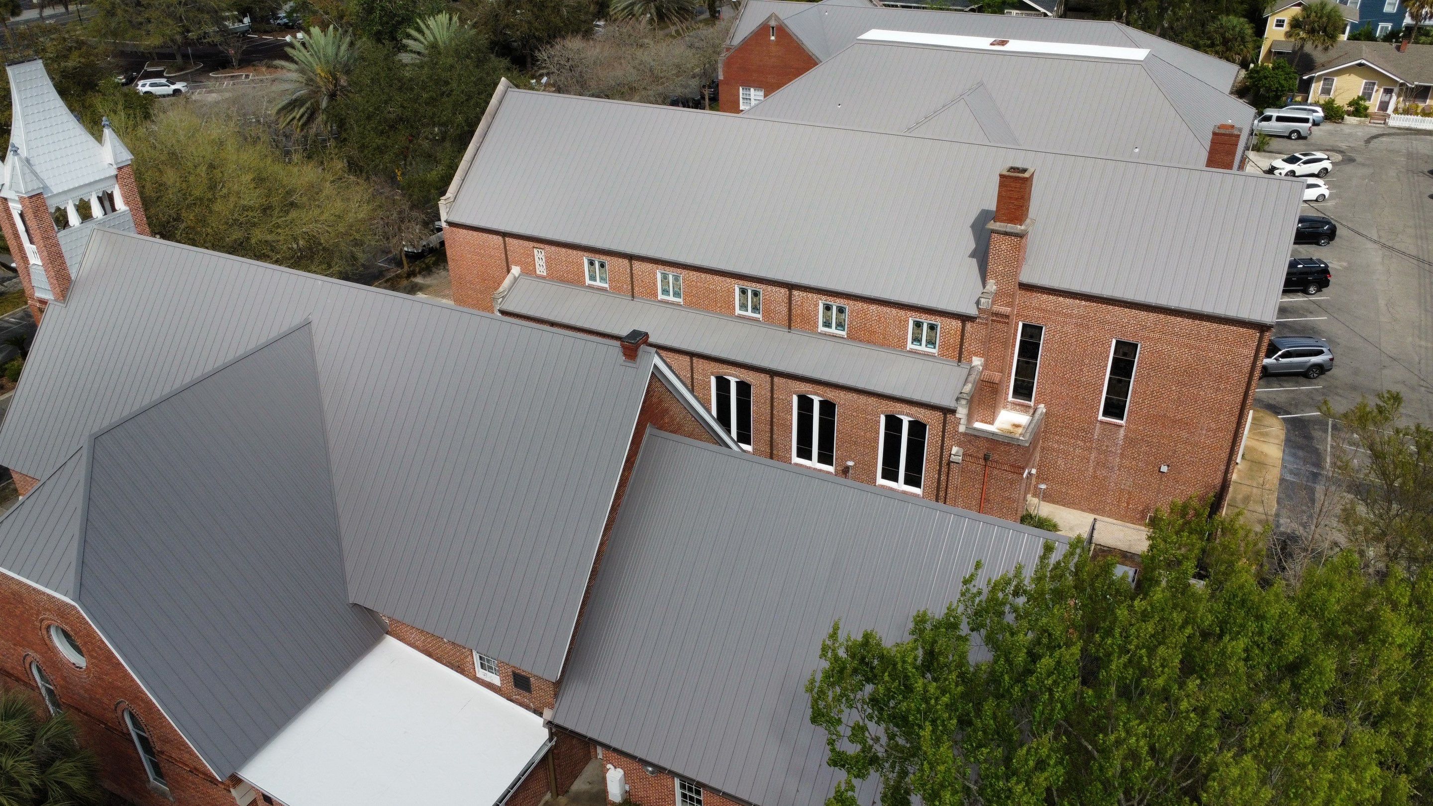 Gray shingle roof with a black vent near a brick wall and green trees in the background