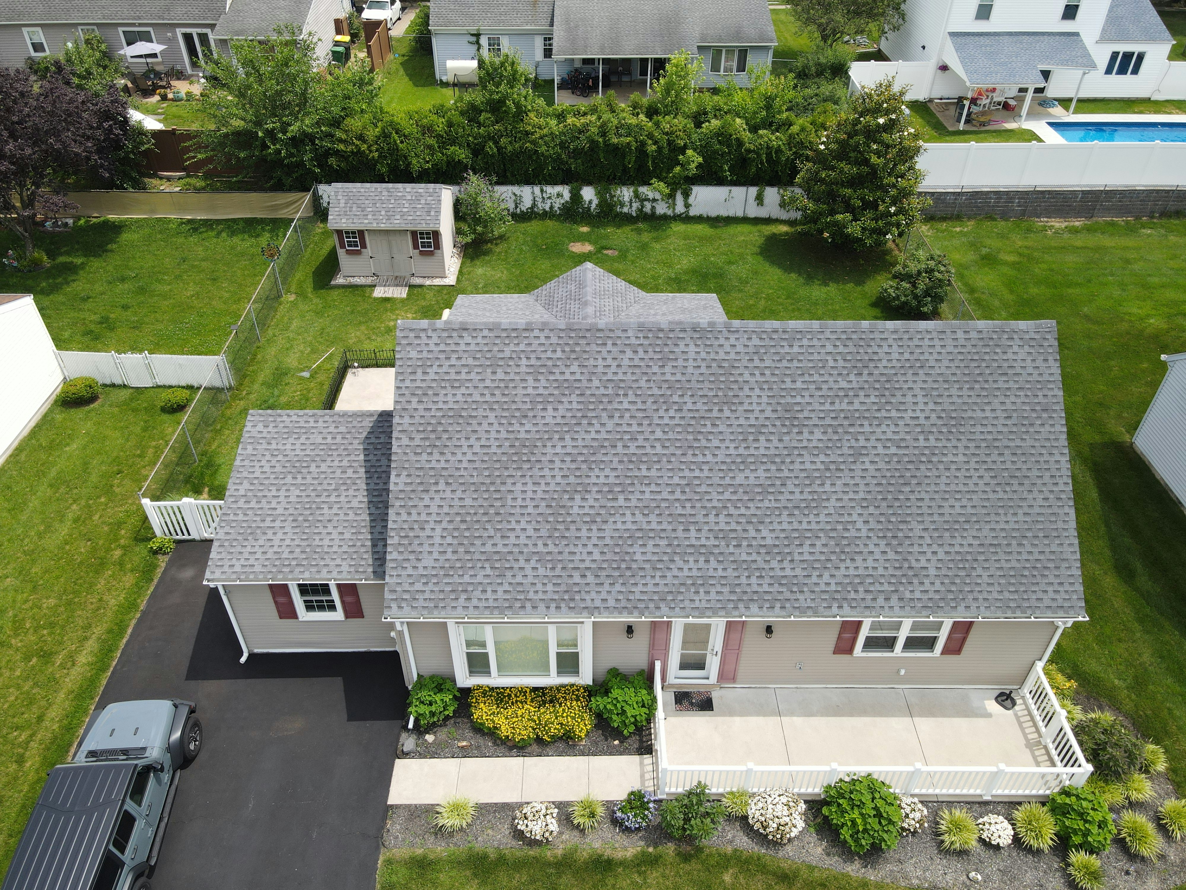 Gray shingle roof with a black vent near a brick wall and green trees in the background