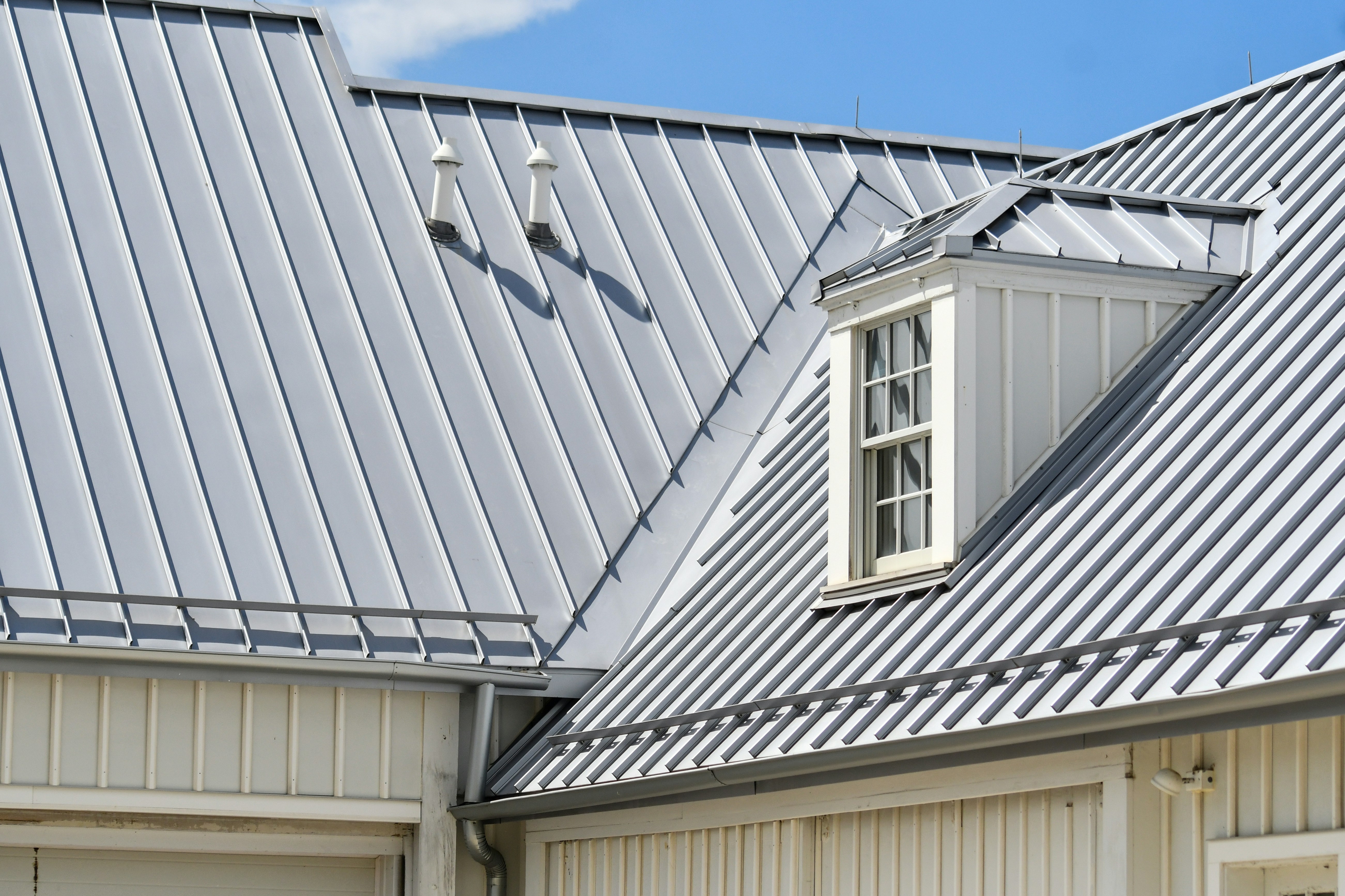 Gray shingle roof with a black vent near a brick wall and green trees in the background