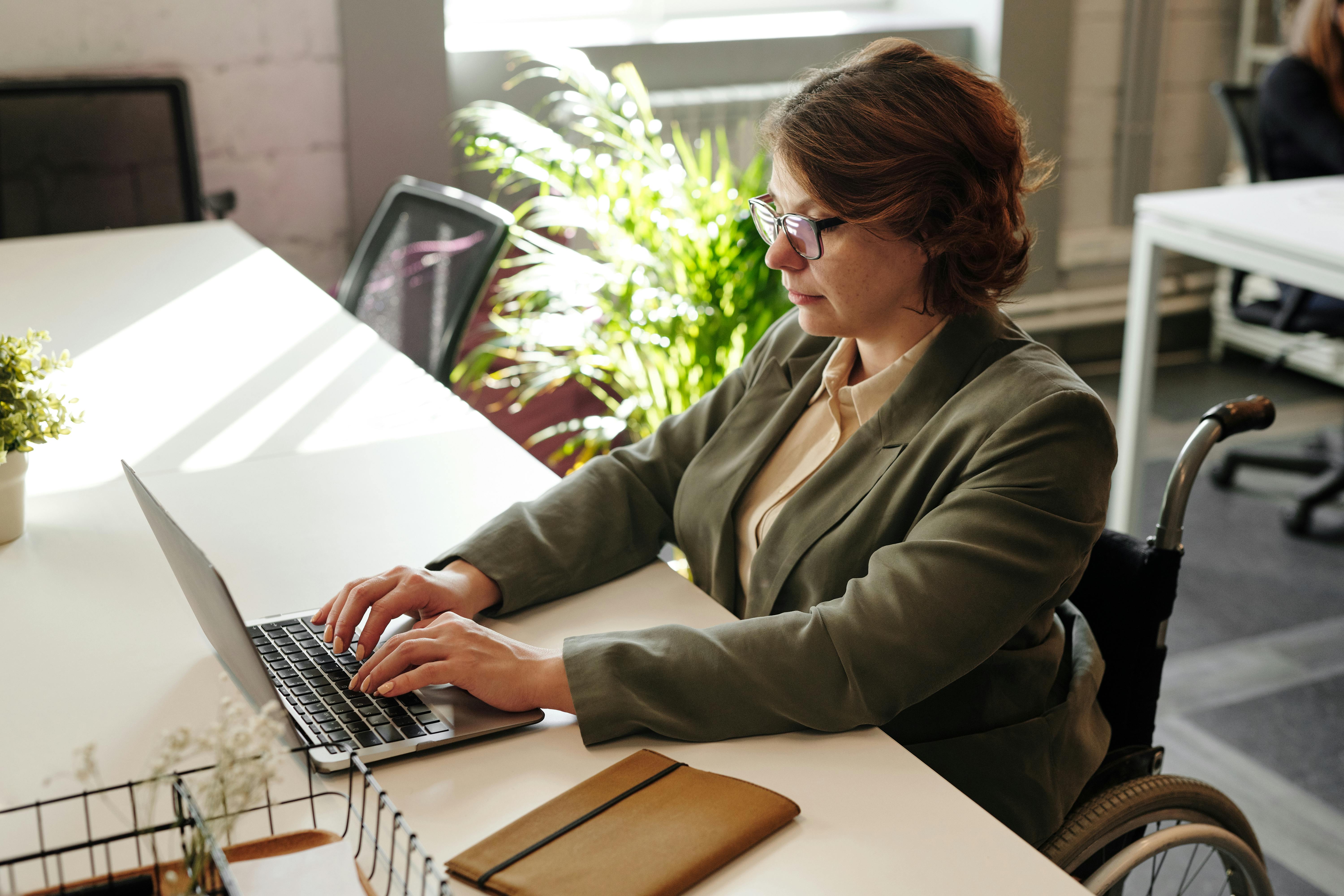 Woman wearing headphones and glasses, smiling while looking at a computer screen.