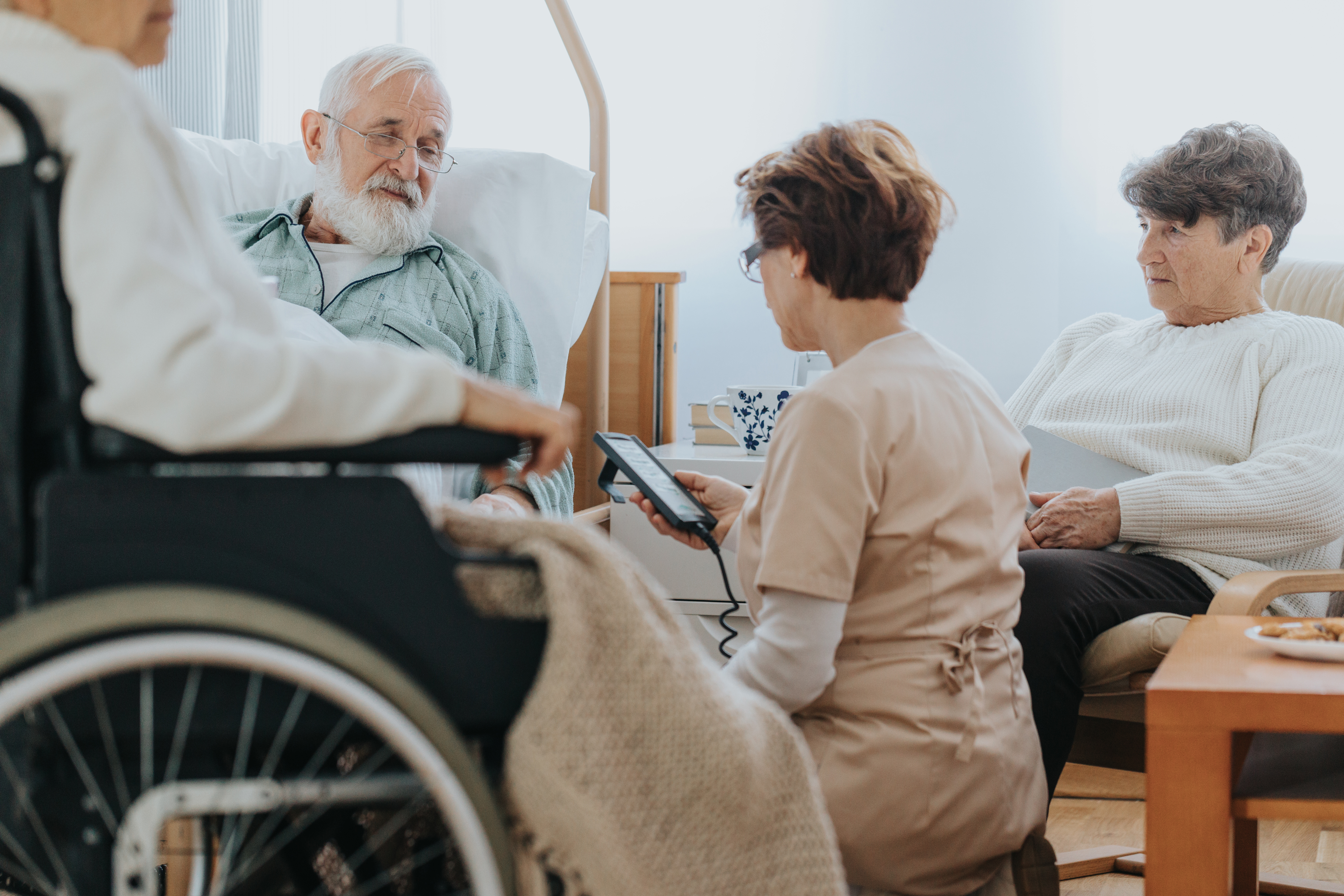 Elderly man in a hospital bed with a nurse and two visitors.
