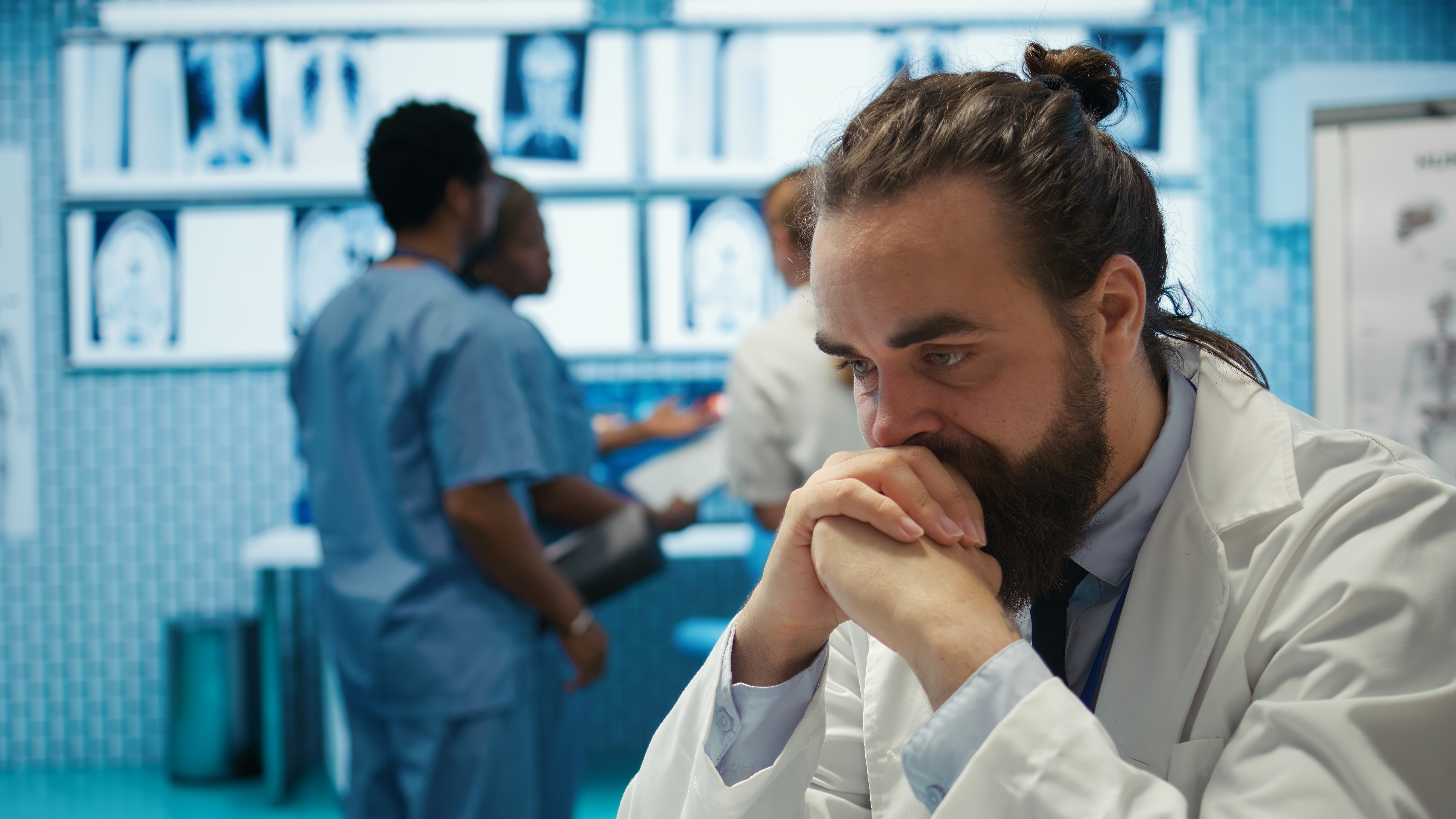 Doctor in a lab coat looking thoughtful with medical staff in the background