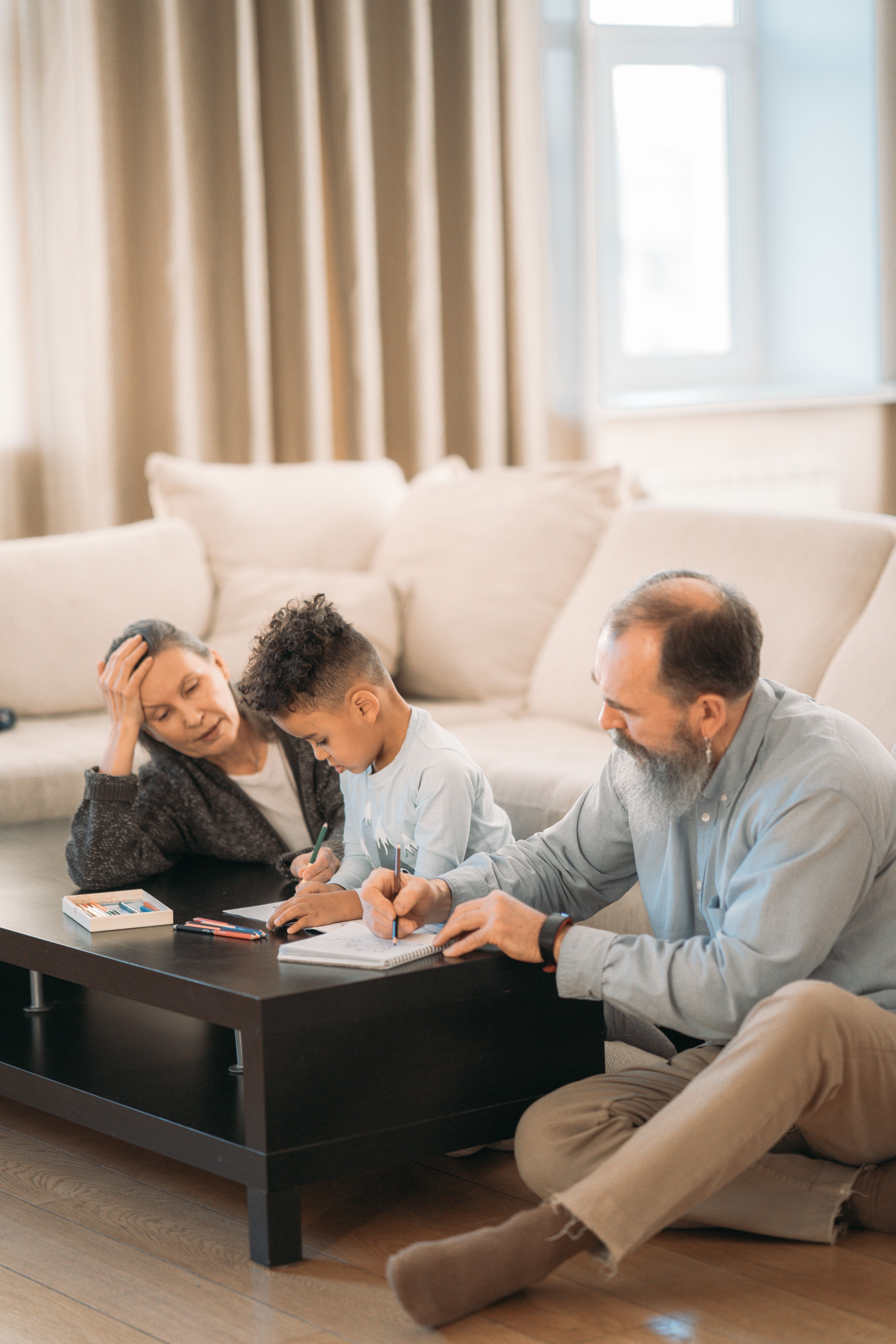 Grandparents and child sitting on the floor doing homework together in a cozy living room.