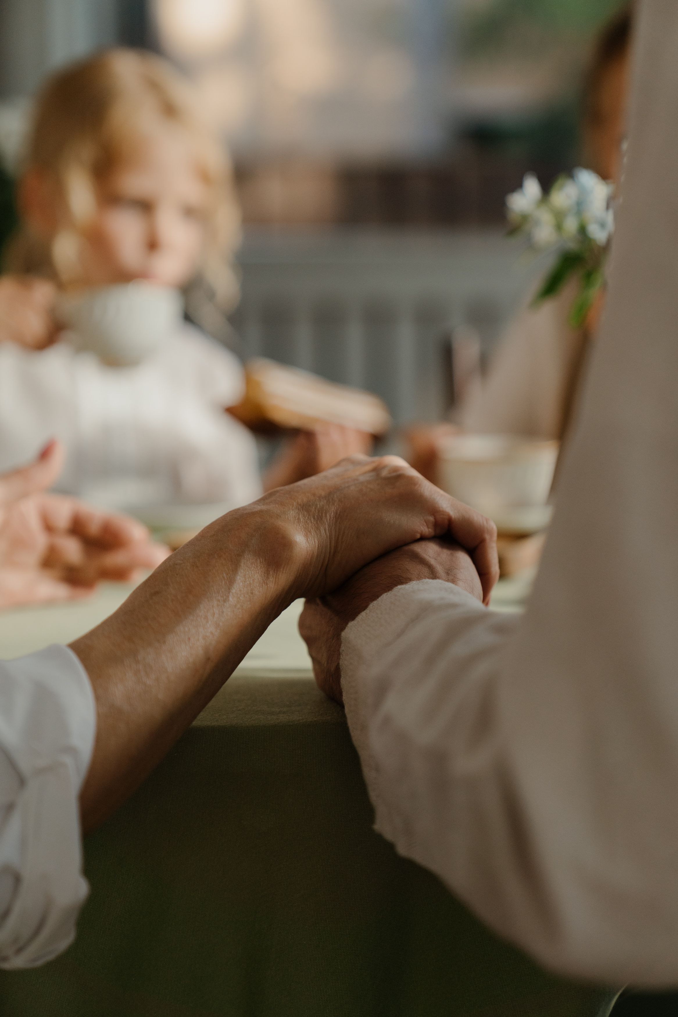 Elderly hands holding across a table with a child in the background