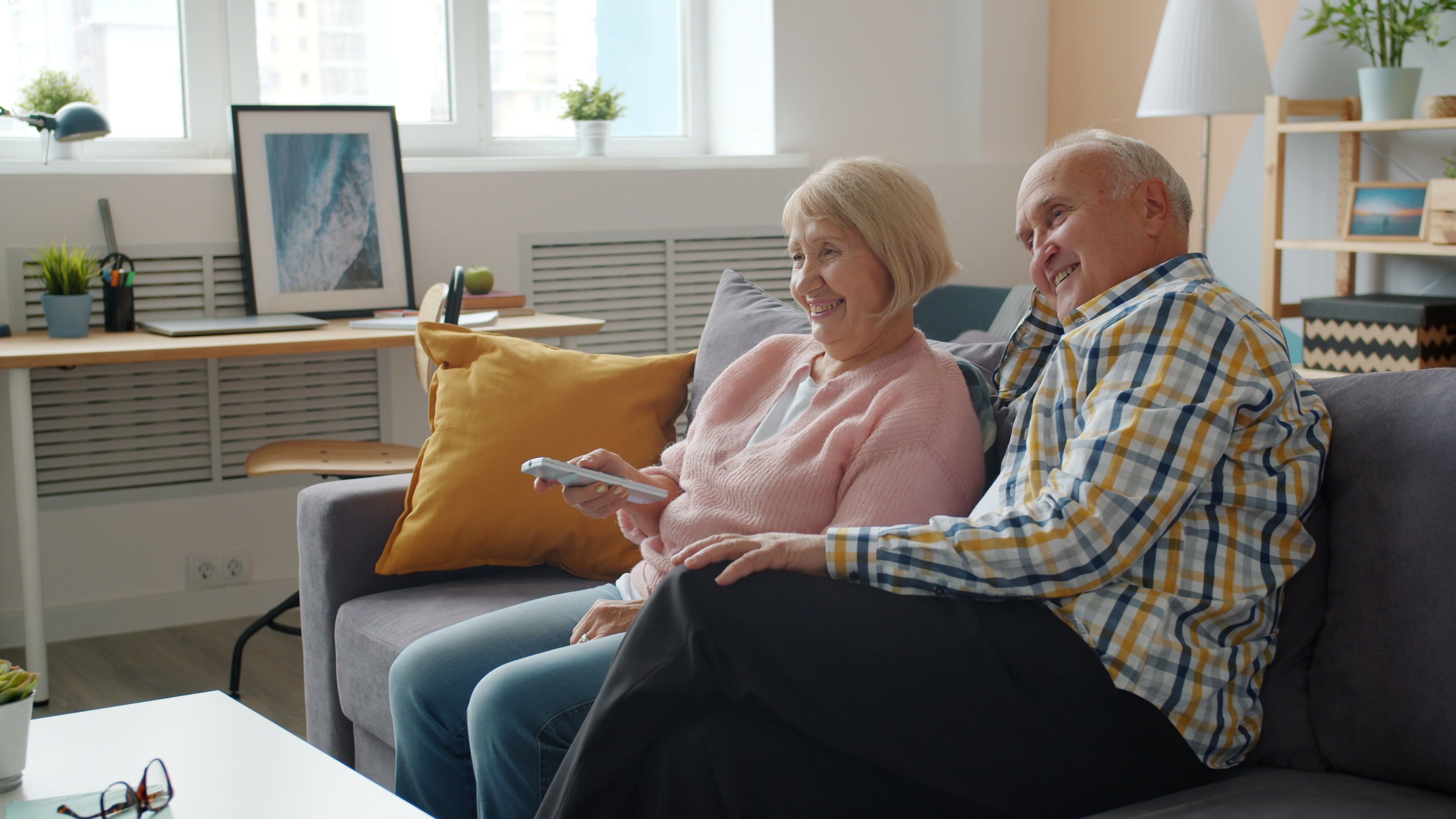 Smiling elderly couple sitting on a couch watching TV together.