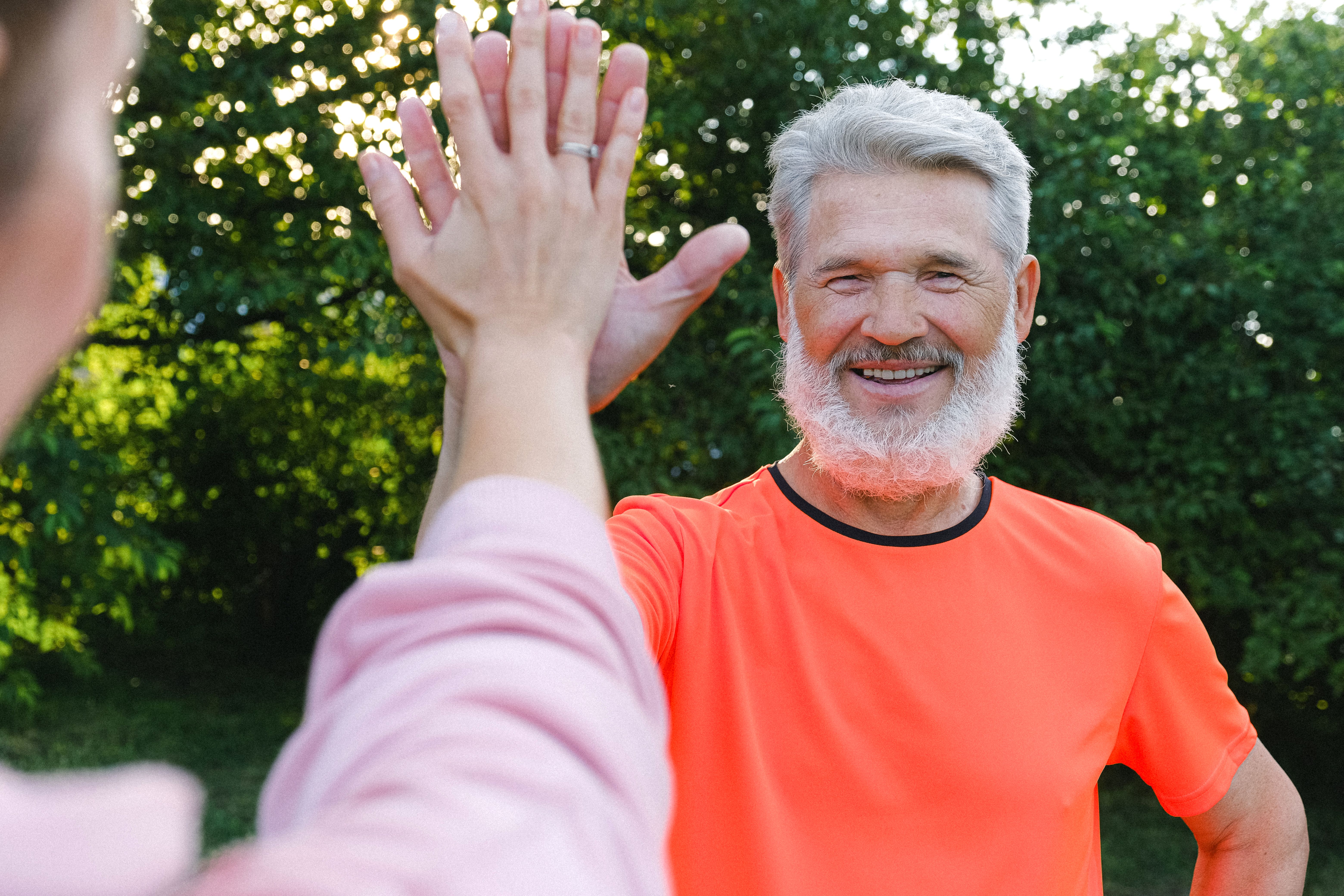 Older man in an orange shirt giving a high-five outdoors.