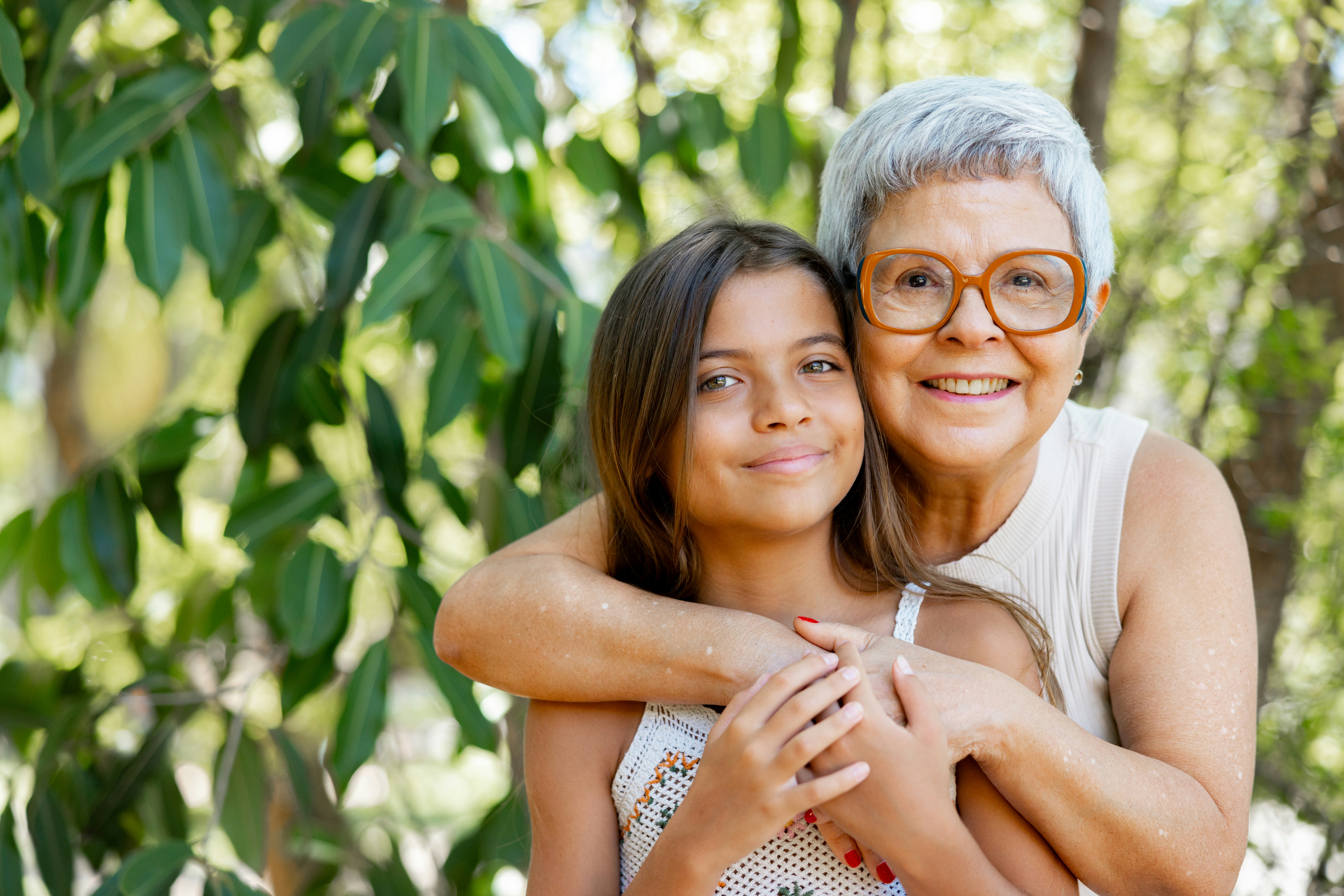 Smiling elderly woman with glasses hugging a young girl outdoors
