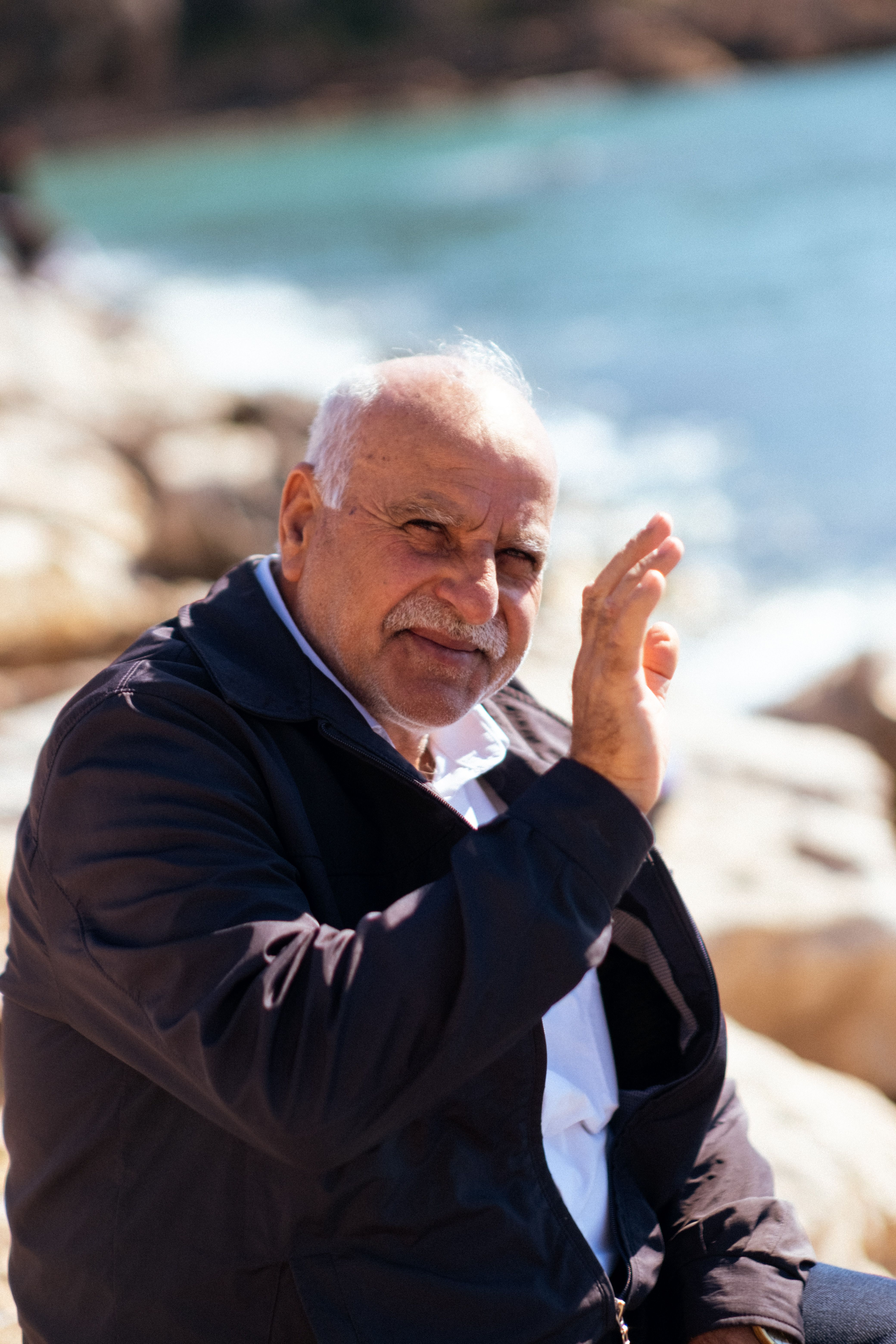 Elderly man smiling and waving by the seaside