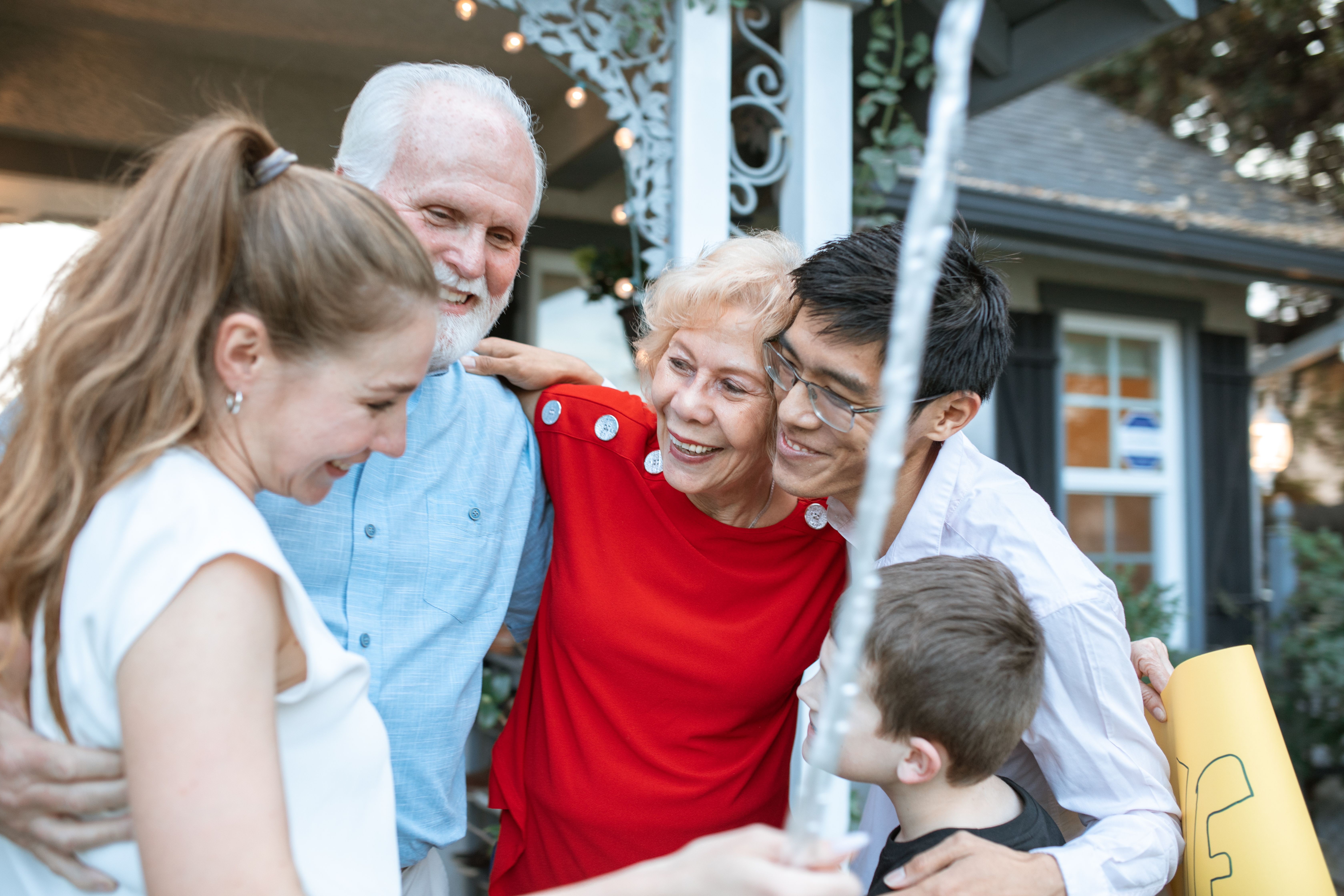 A diverse group of people embracing and smiling outside a house.