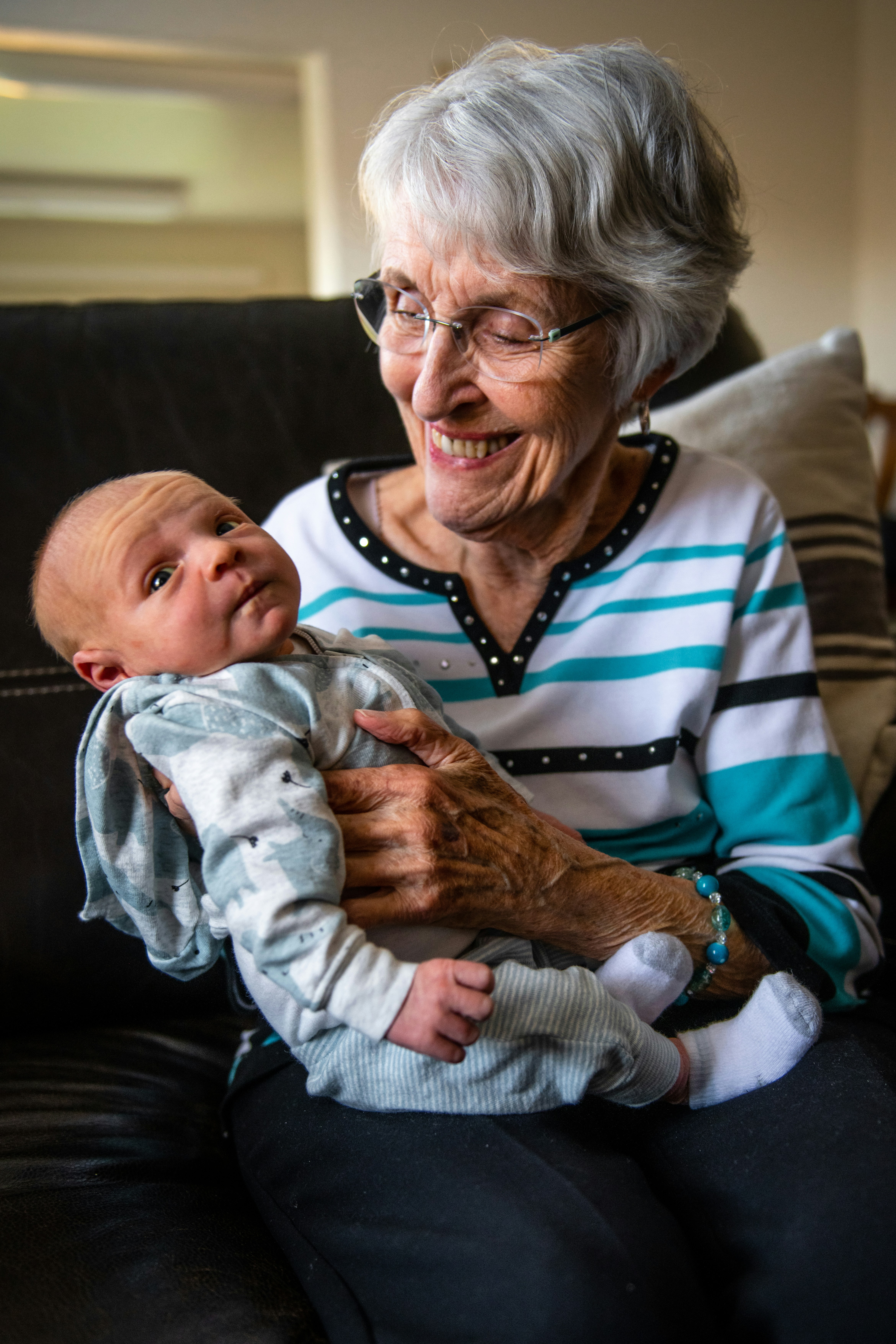 Elderly woman smiling while holding a newborn baby on a couch