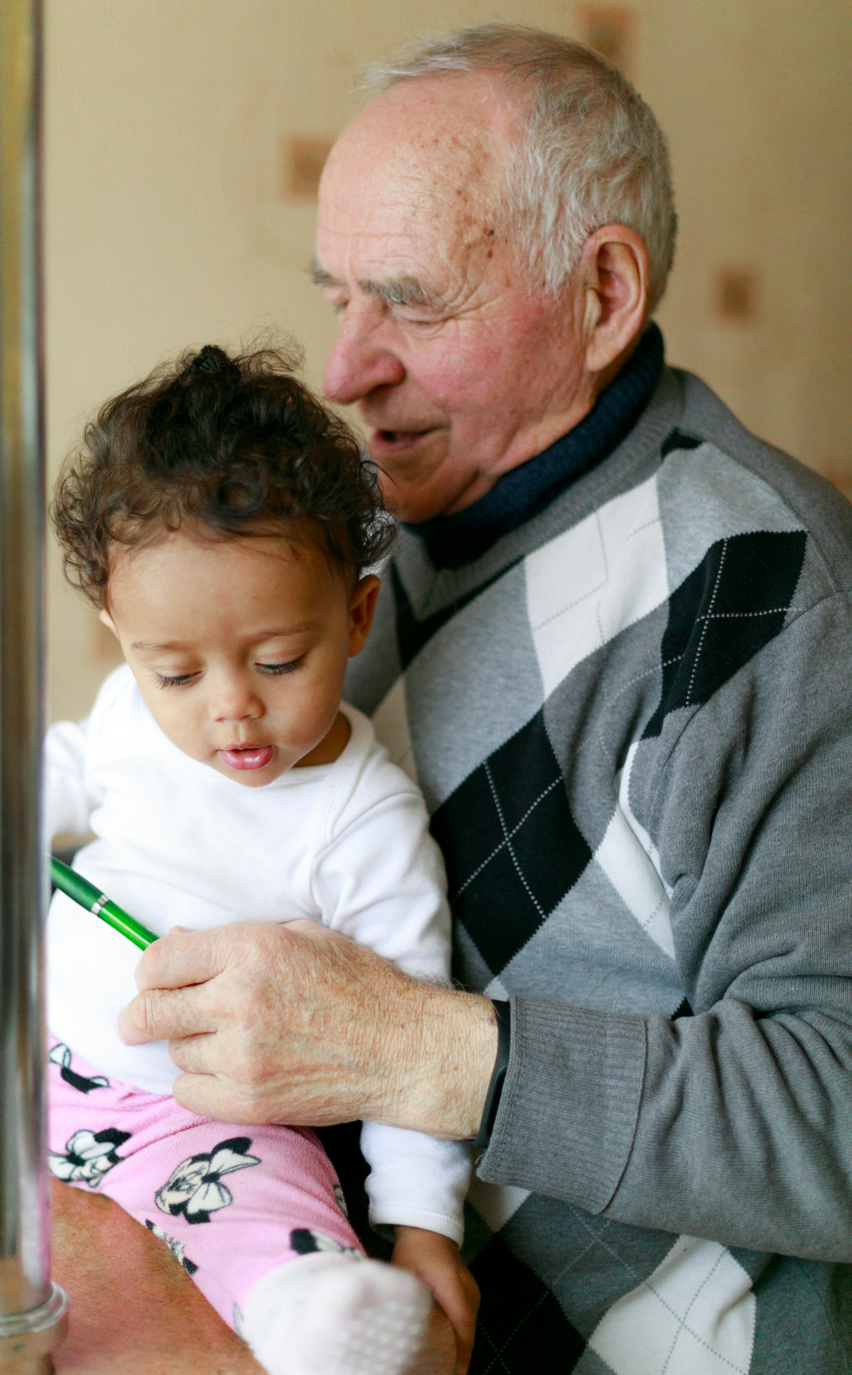 Elderly man holding a toddler on his lap, both looking at a pen.