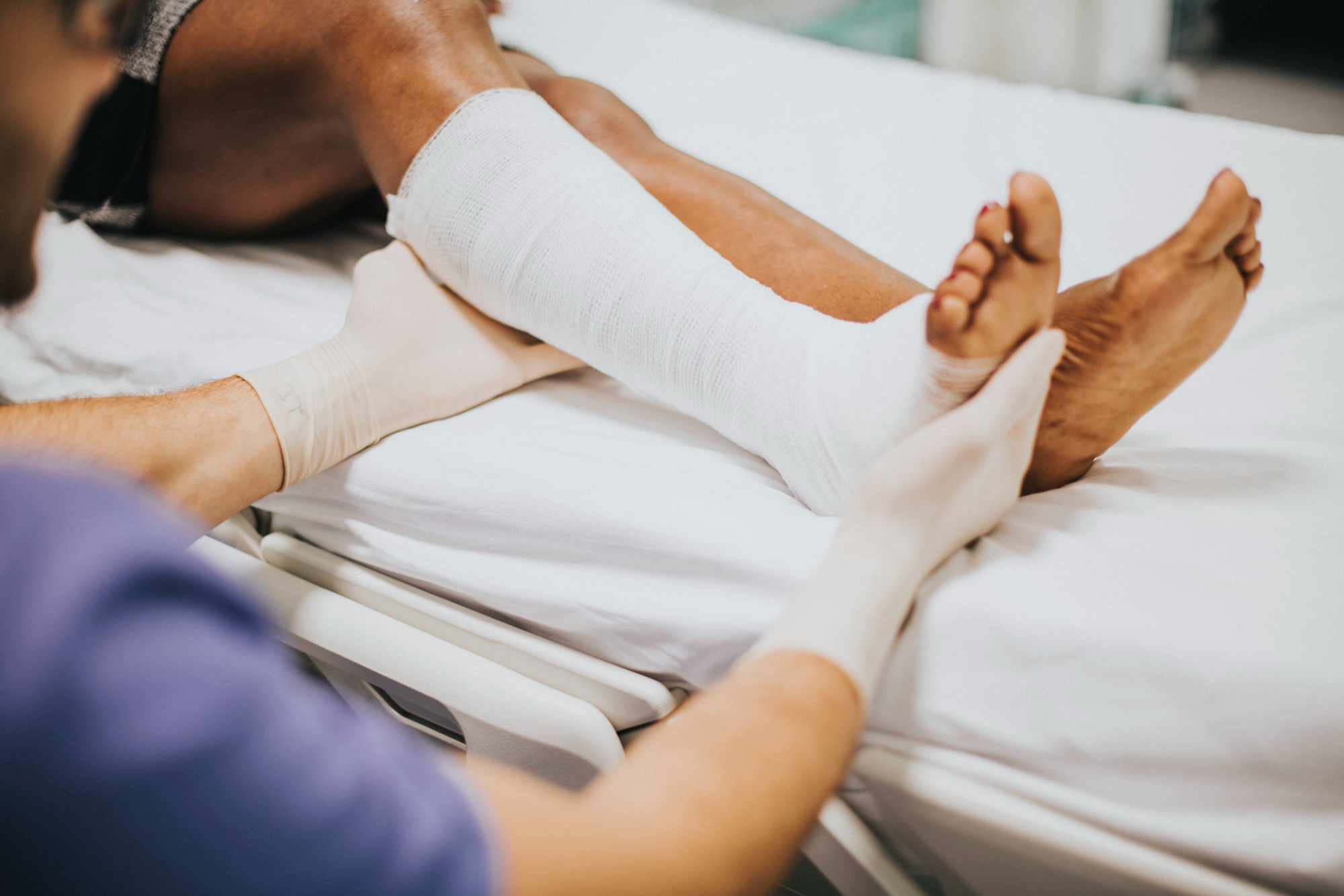 Medical professional examining a patient's bandaged leg in a hospital setting