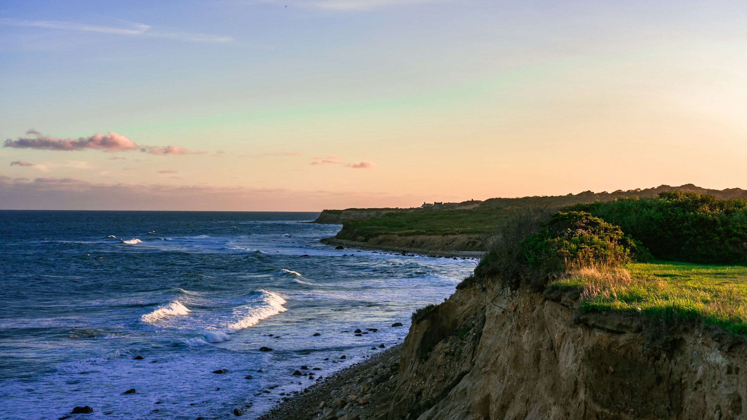 Scenic view of a coastal cliff with waves crashing against the shore at sunset