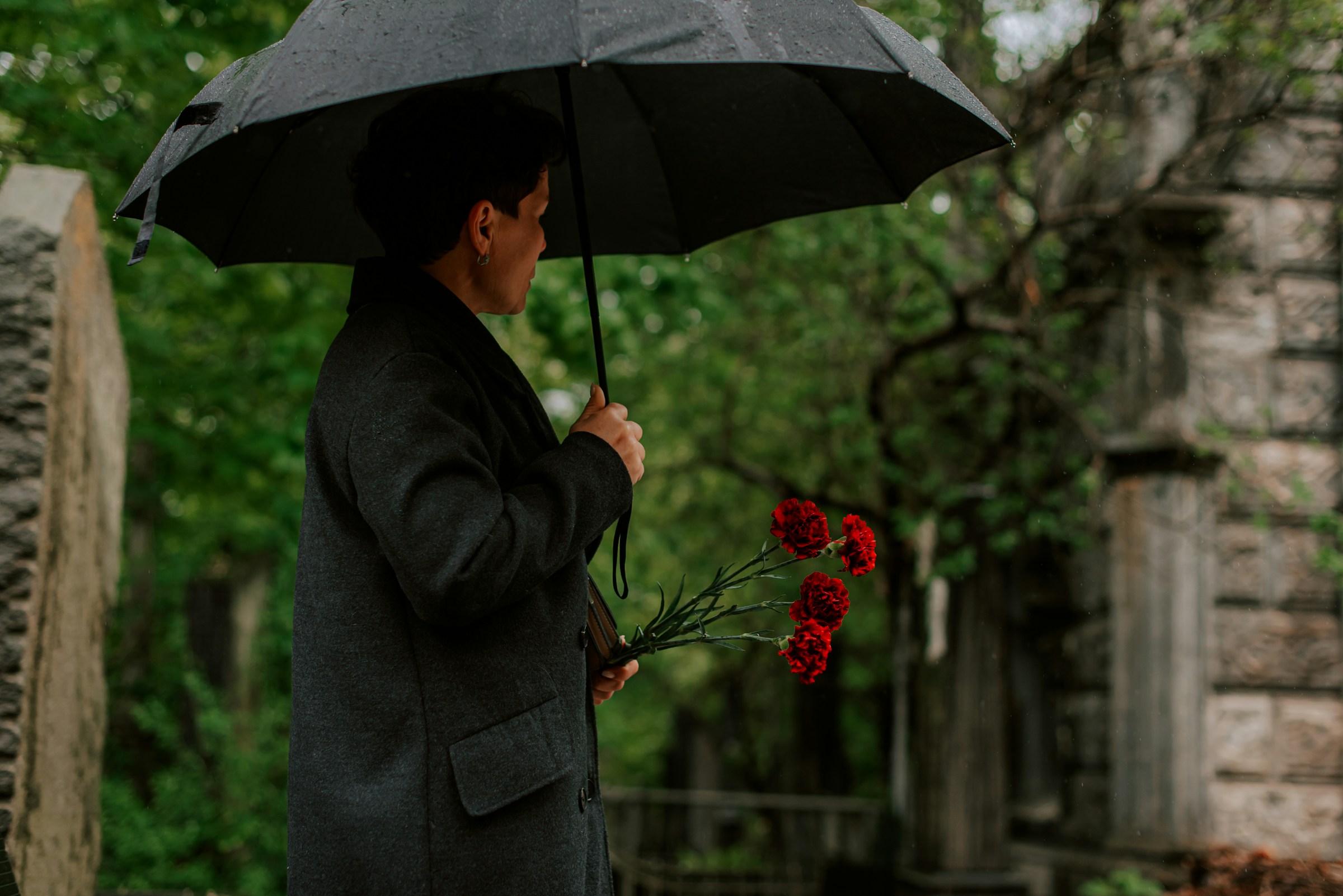 Person holding an umbrella and red flowers in a cemetery