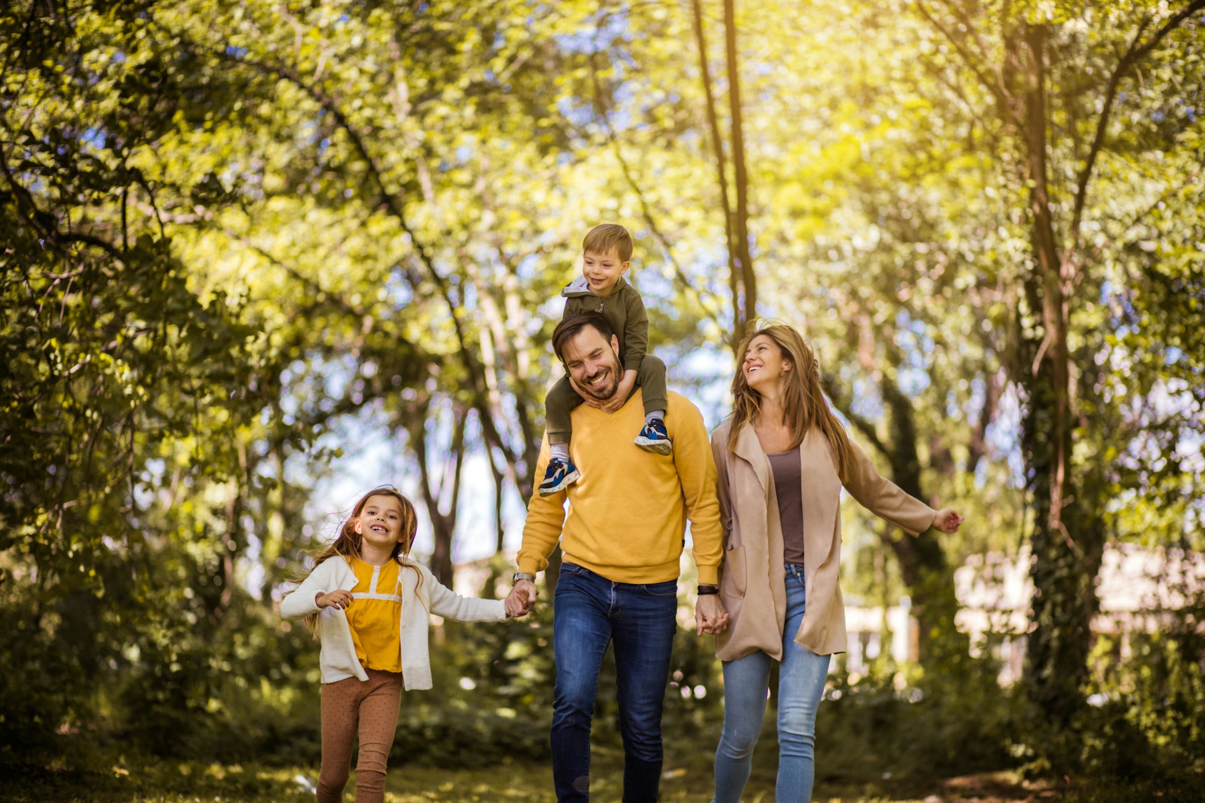 Happy family walking together in a sunny park with trees in the background