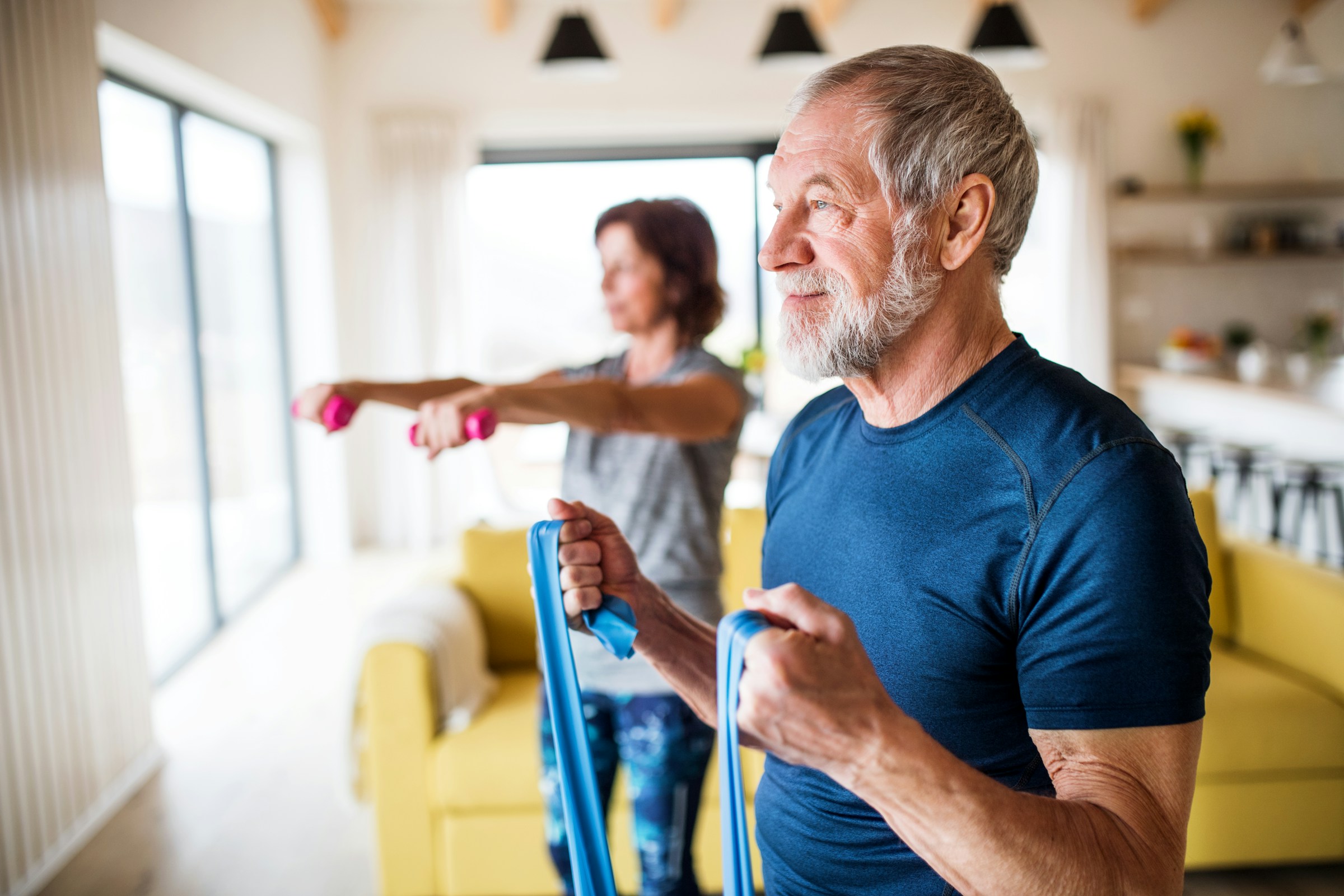 Older adults exercising with resistance bands and dumbbells in a bright living room