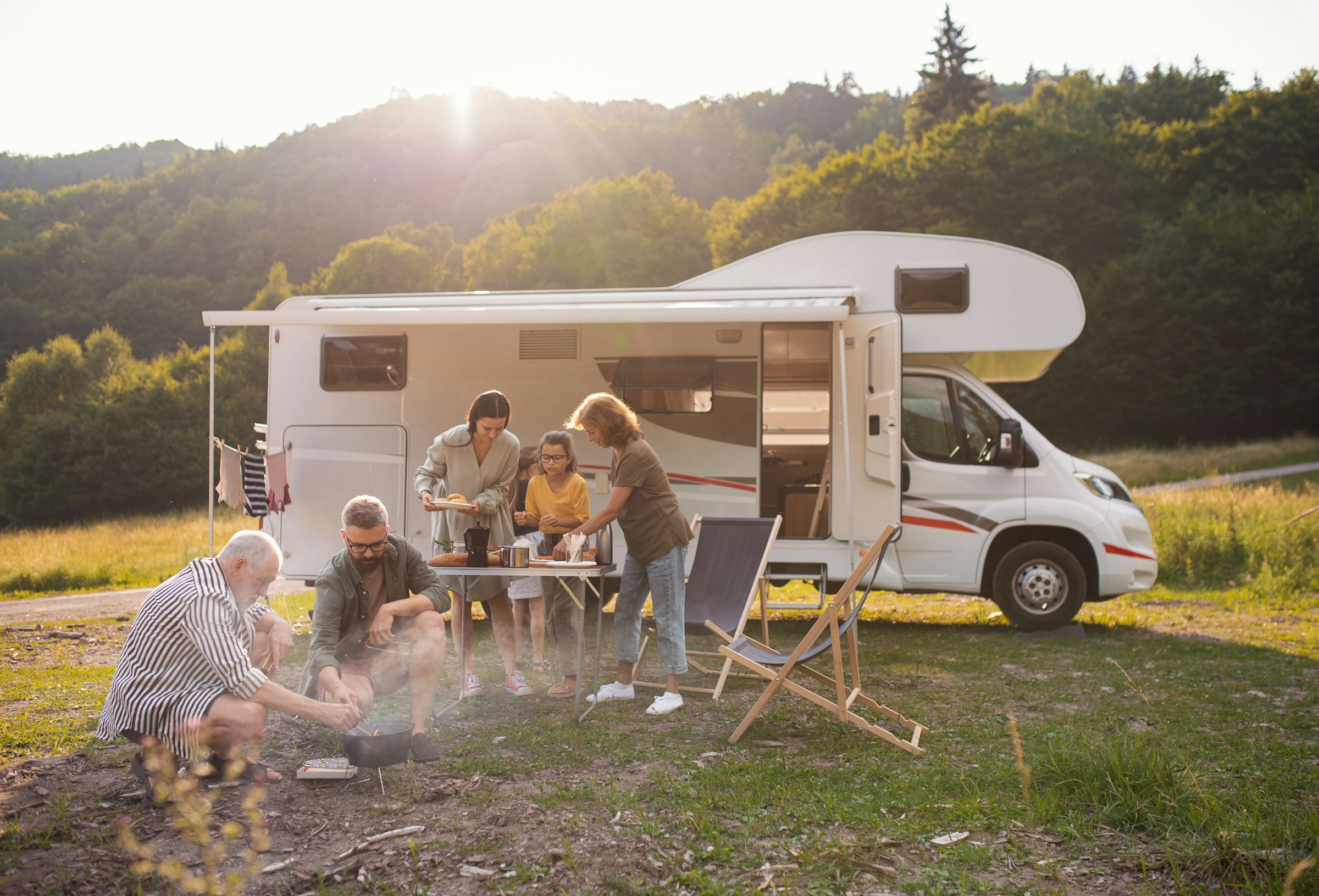 Family enjoying a barbecue next to a camper van in a scenic outdoor setting.