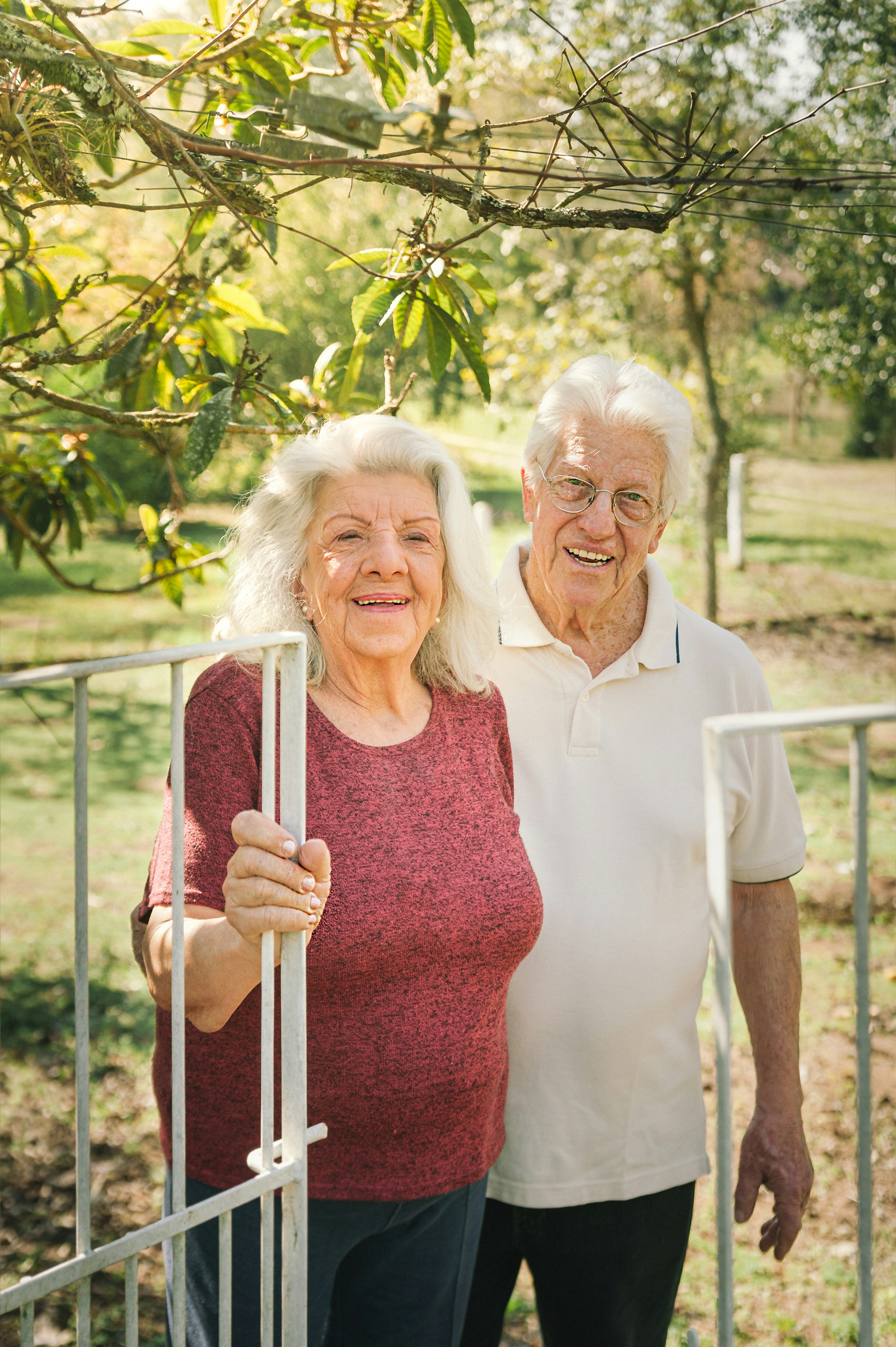 Elderly couple smiling in a garden setting with sunlight filtering through trees