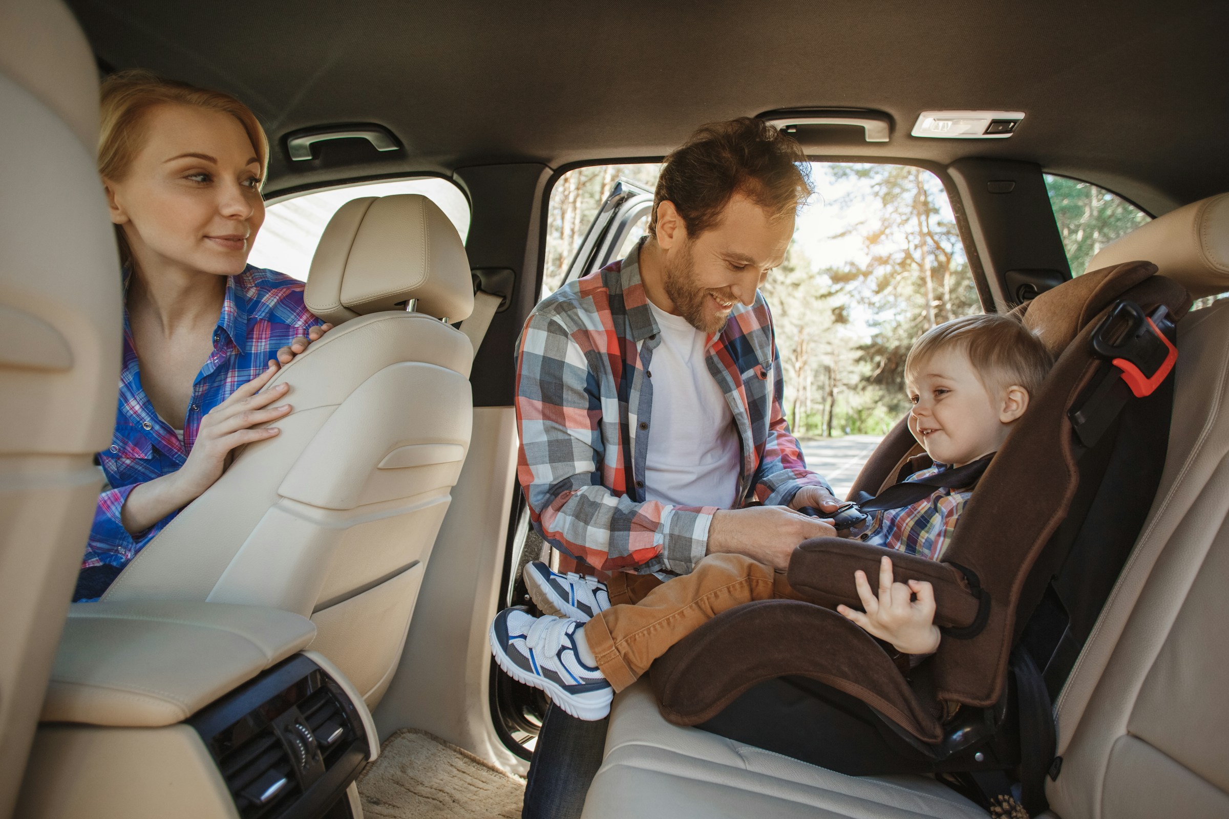 Parents securing their child in a car seat inside a vehicle.