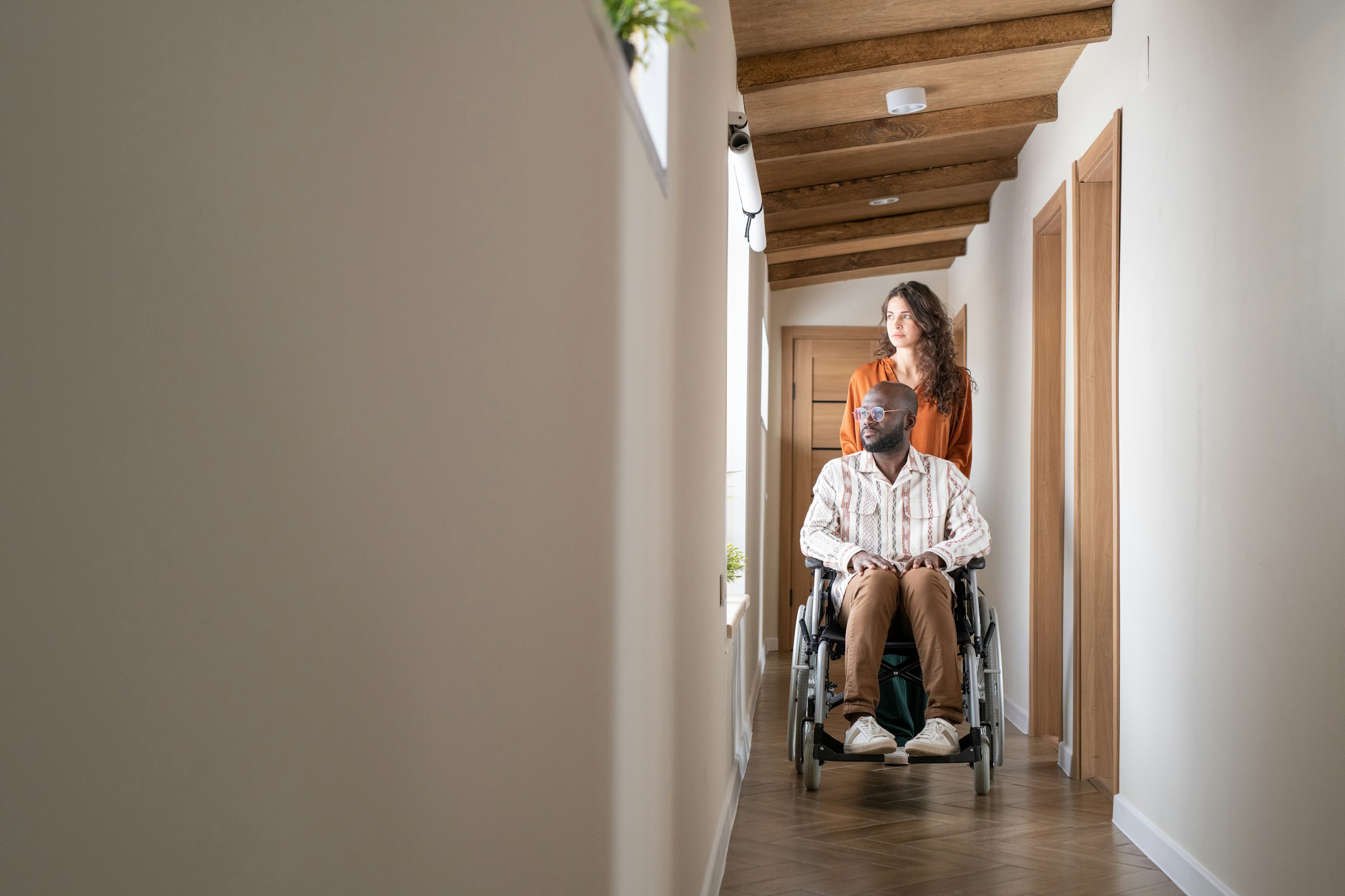 Woman assisting a man in a wheelchair down a hallway