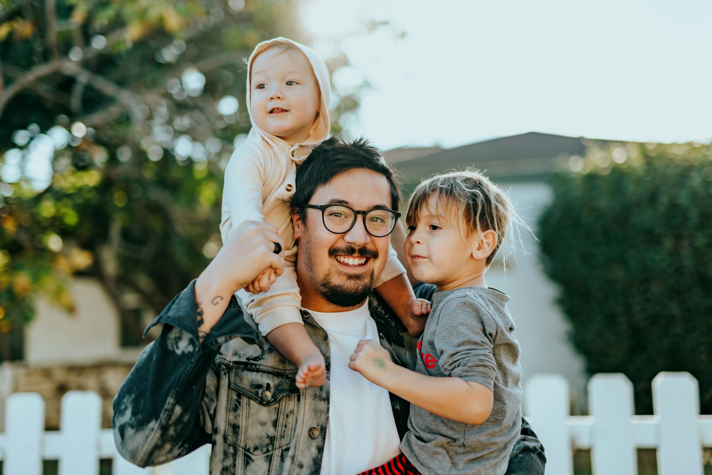 Smiling adult holding two young children in a sunny outdoor setting