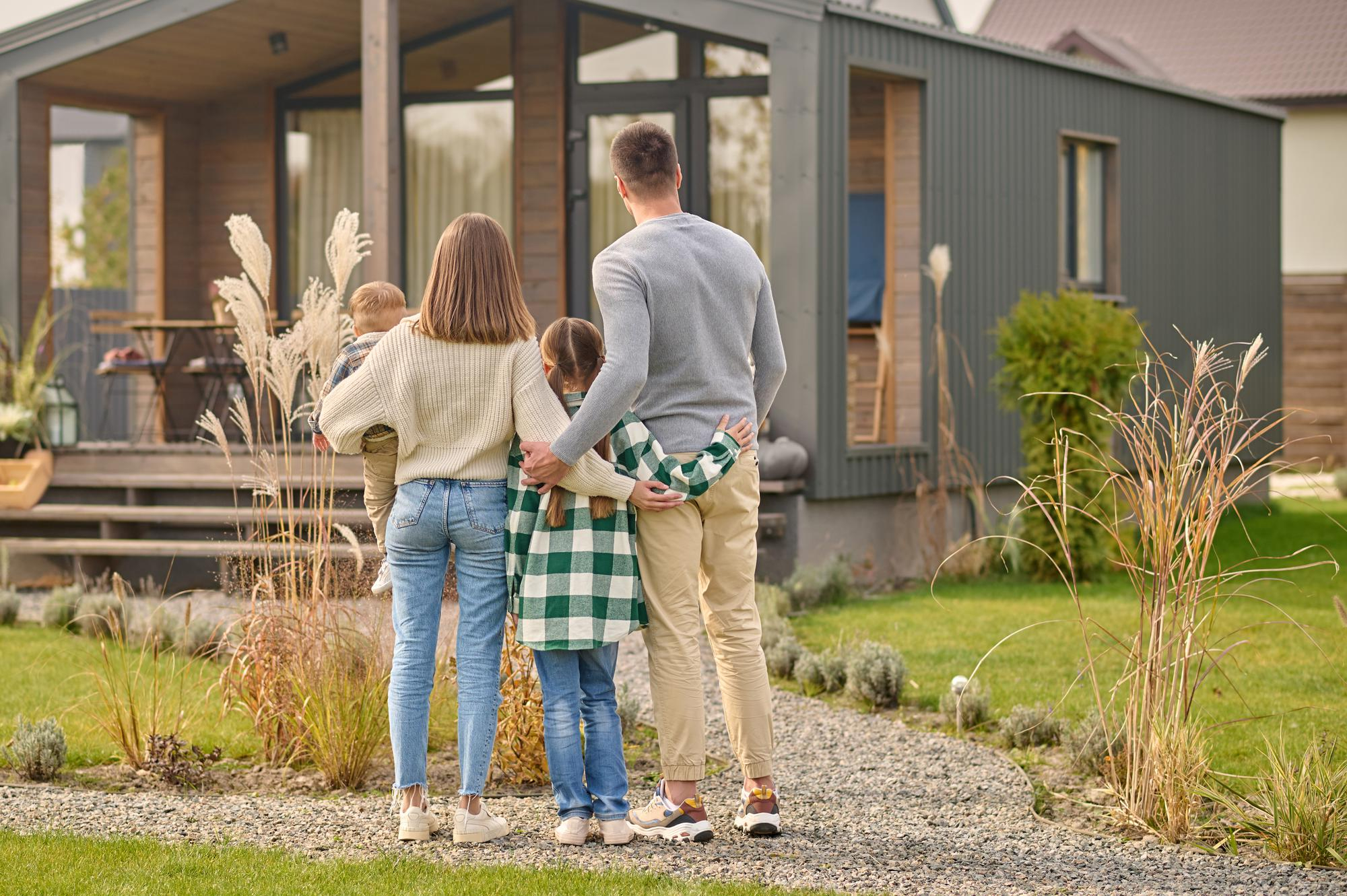 Family of four standing in front of a modern house, looking at the backyard.