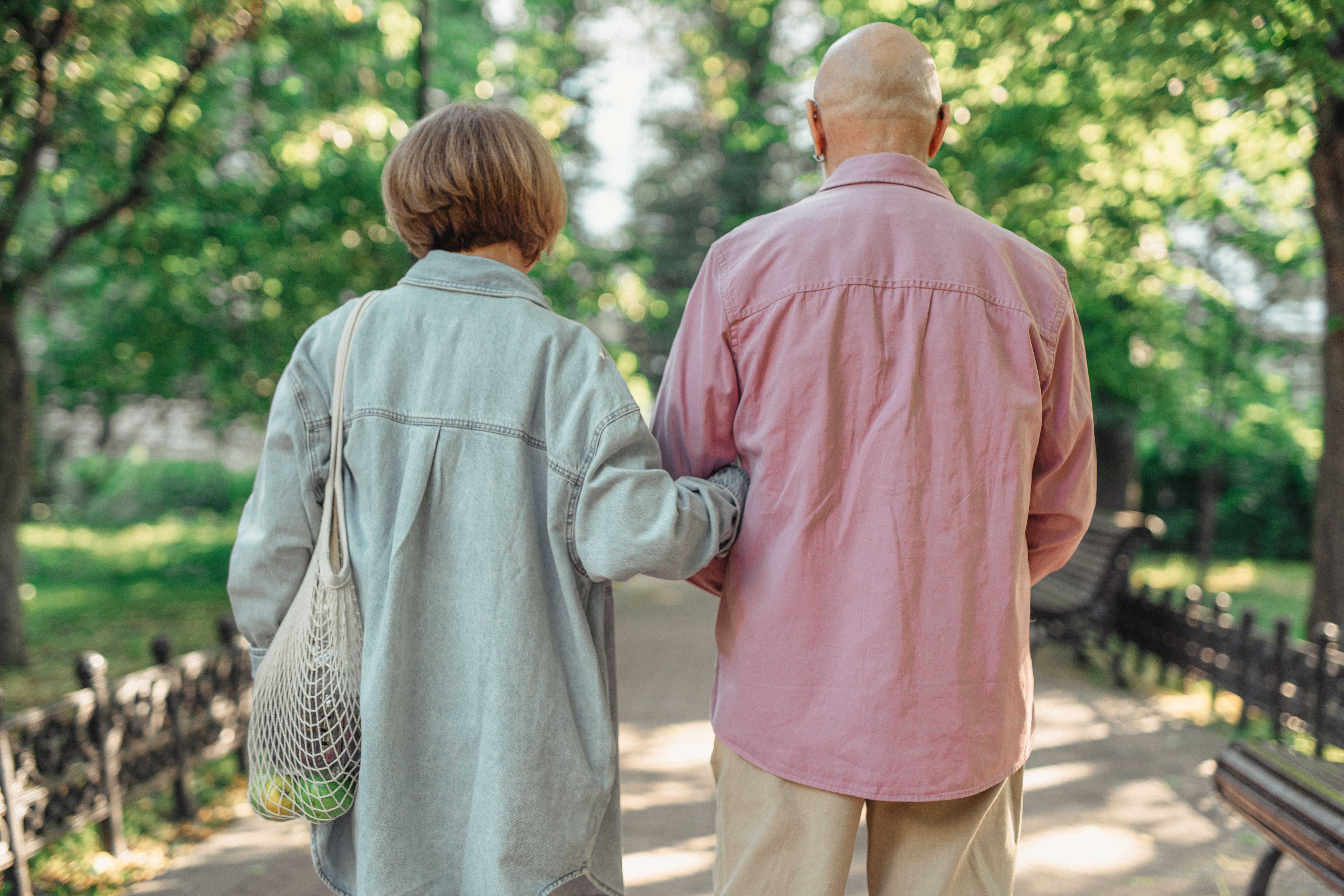 Elderly couple walking arm in arm down a tree-lined path