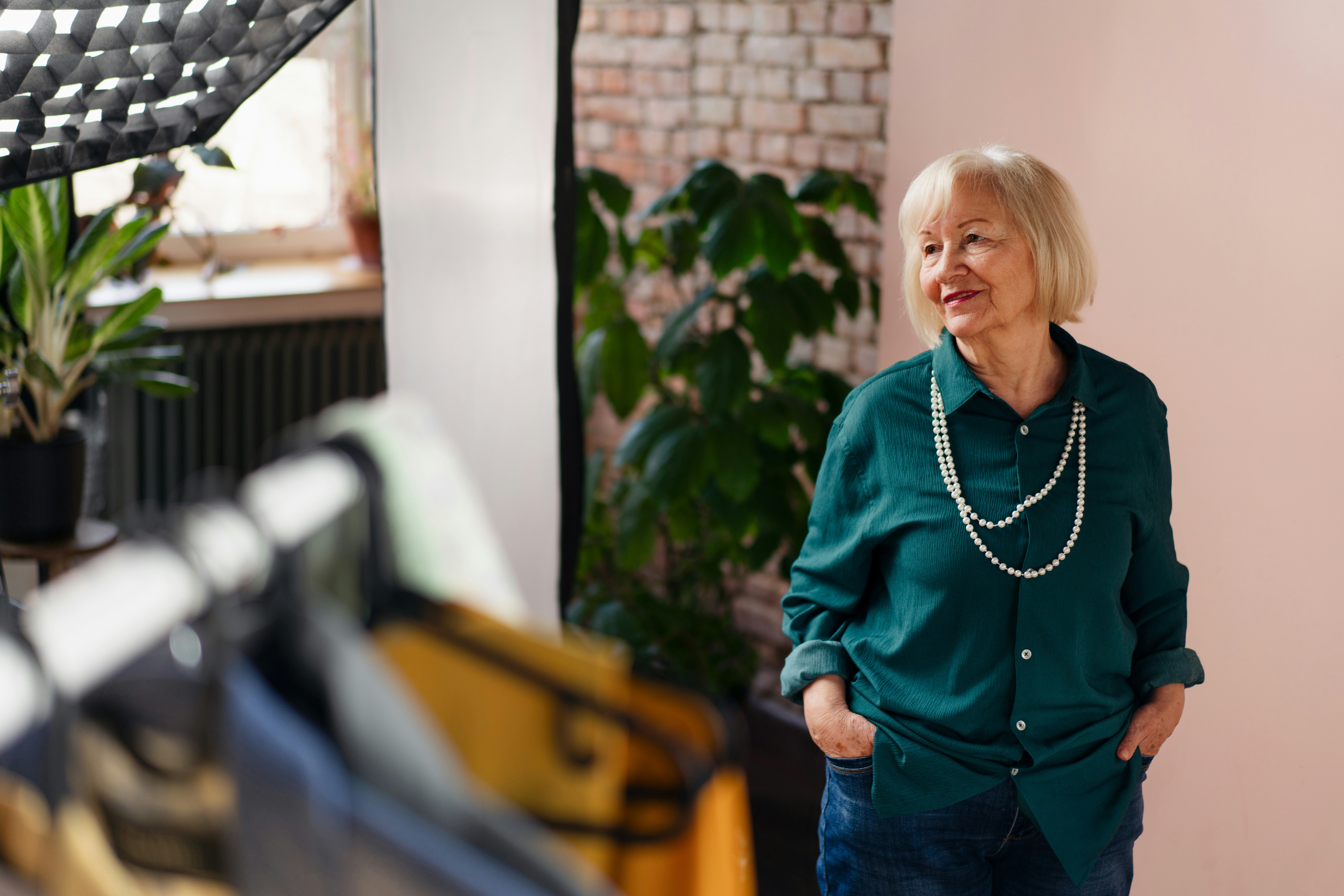 Elderly woman in a green shirt standing in a room with plants and clothing rack