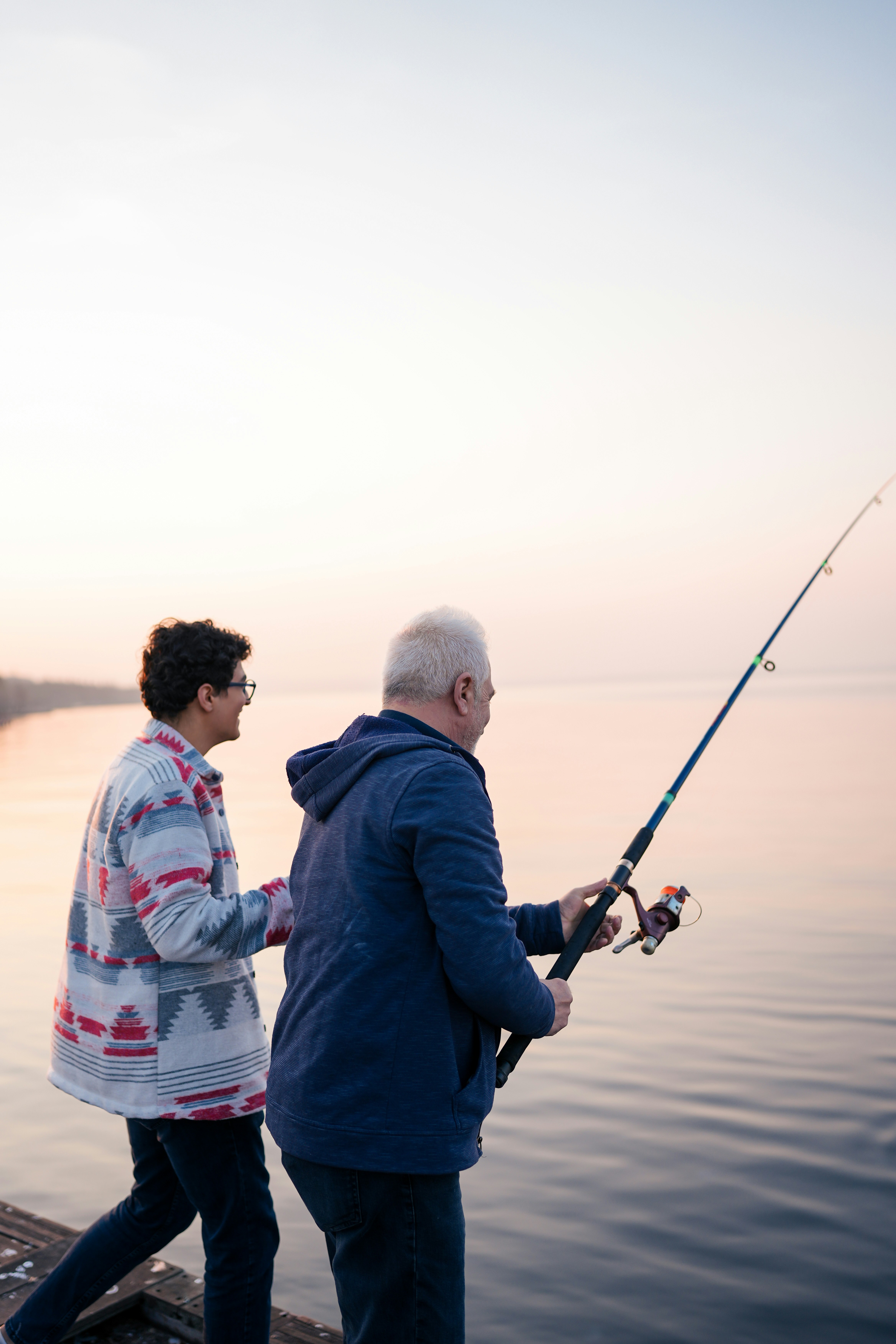 Two people fishing at sunset by a calm lake
