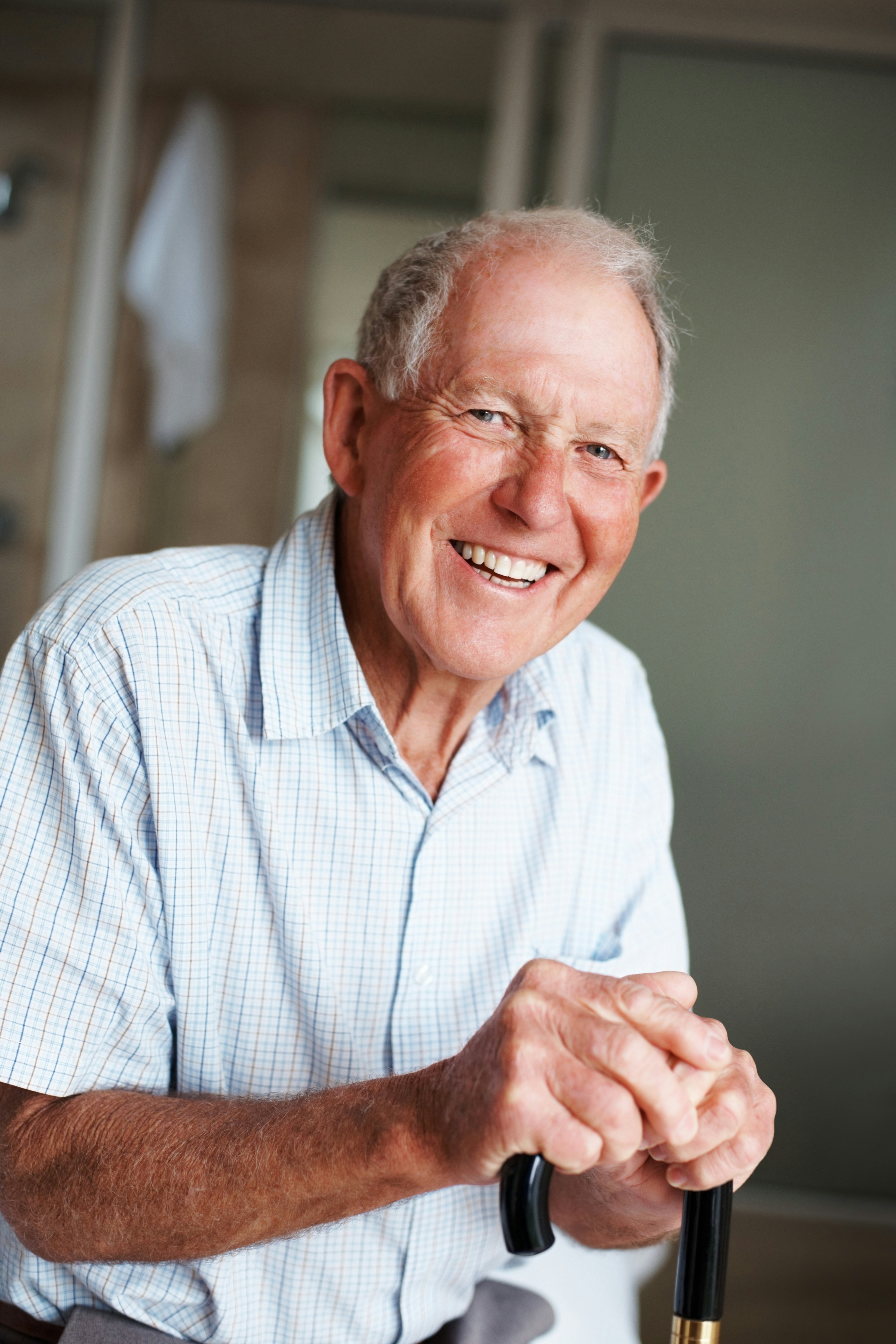 Smiling elderly man holding a cane indoors