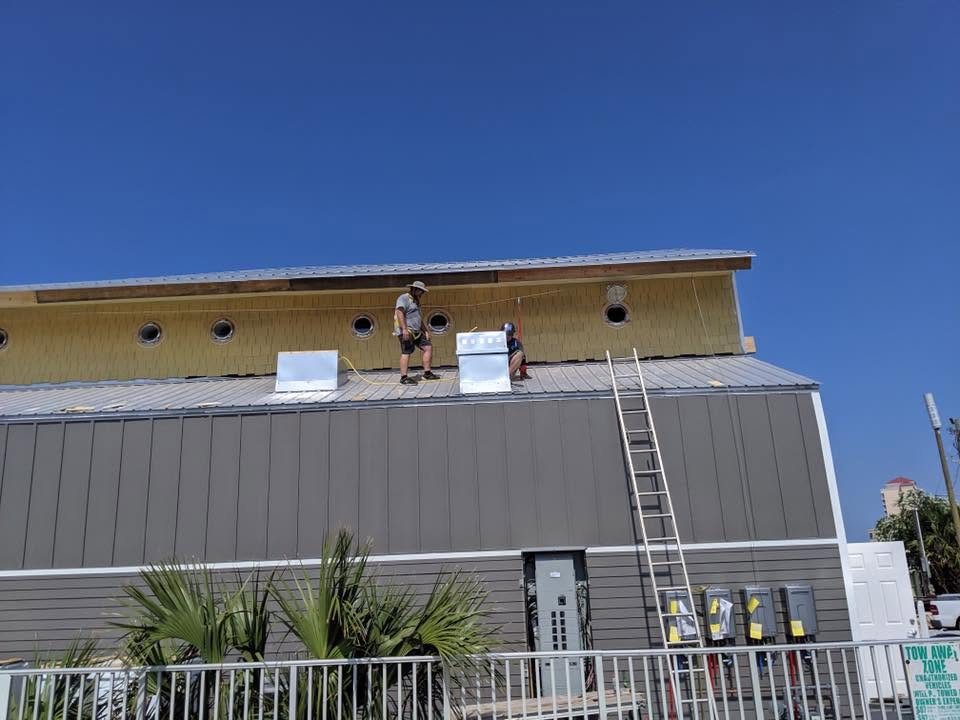 Workers installing siding on a commercial building under clear blue sky