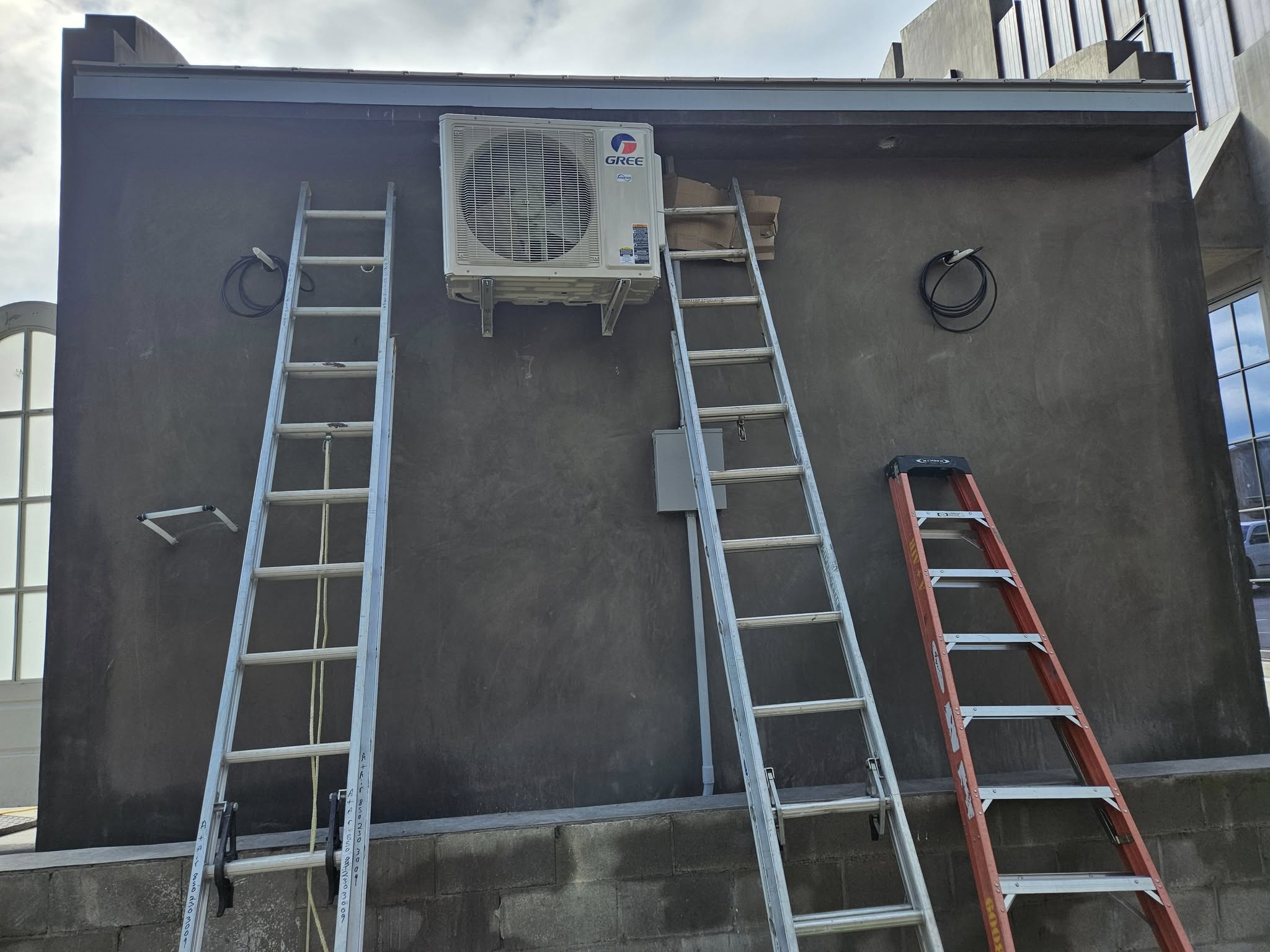 Air conditioning units being installed on a raised platform beside a building near the beach.