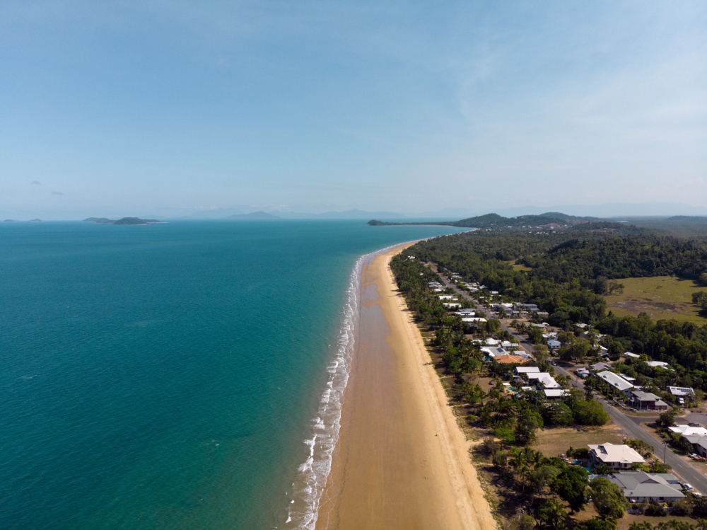 Aerial view of a long sandy beach with turquoise water and adjacent residential area