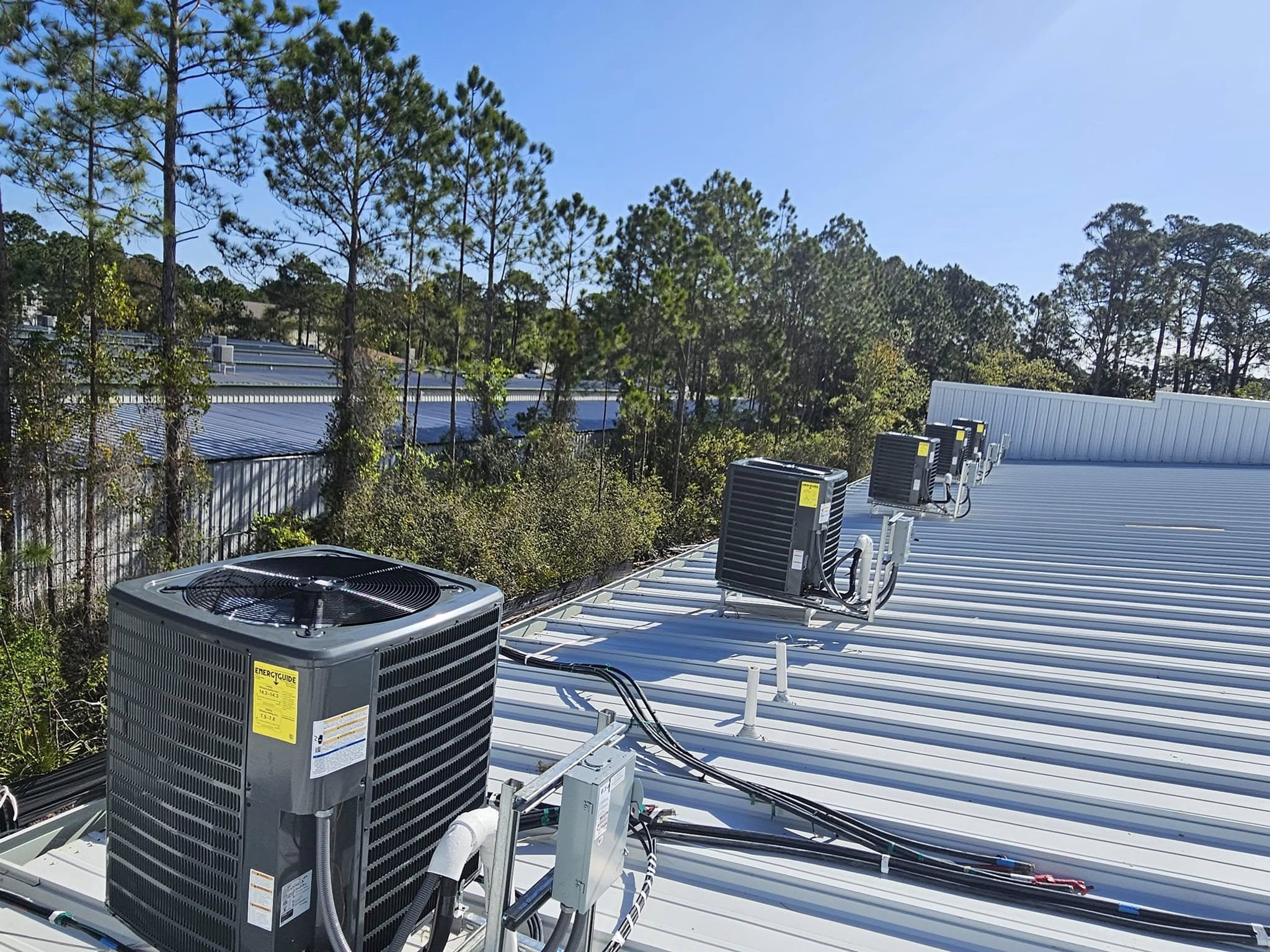Rooftop HVAC units on a metal roof with trees in the background