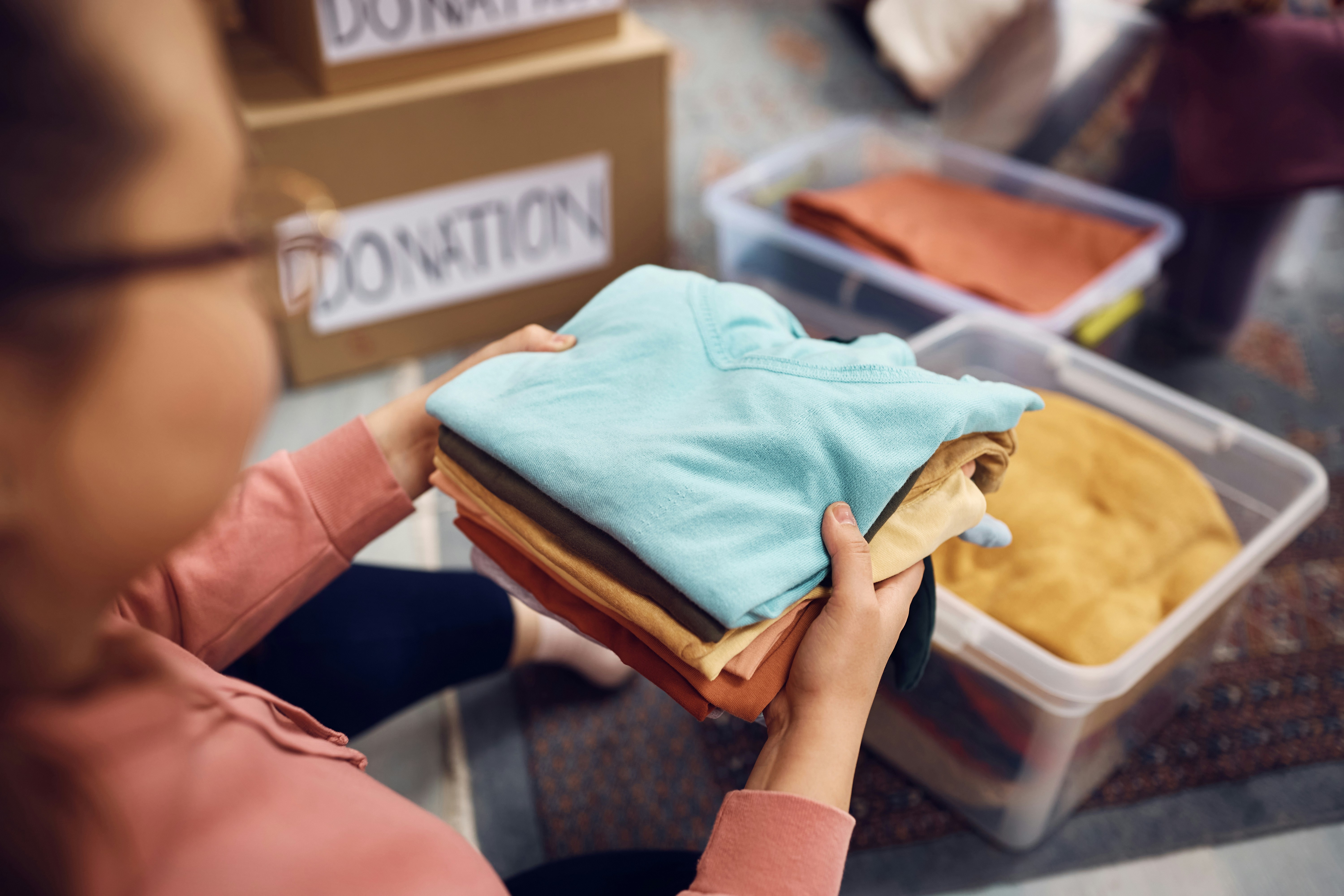 Person holding folded clothes near donation boxes and bins.