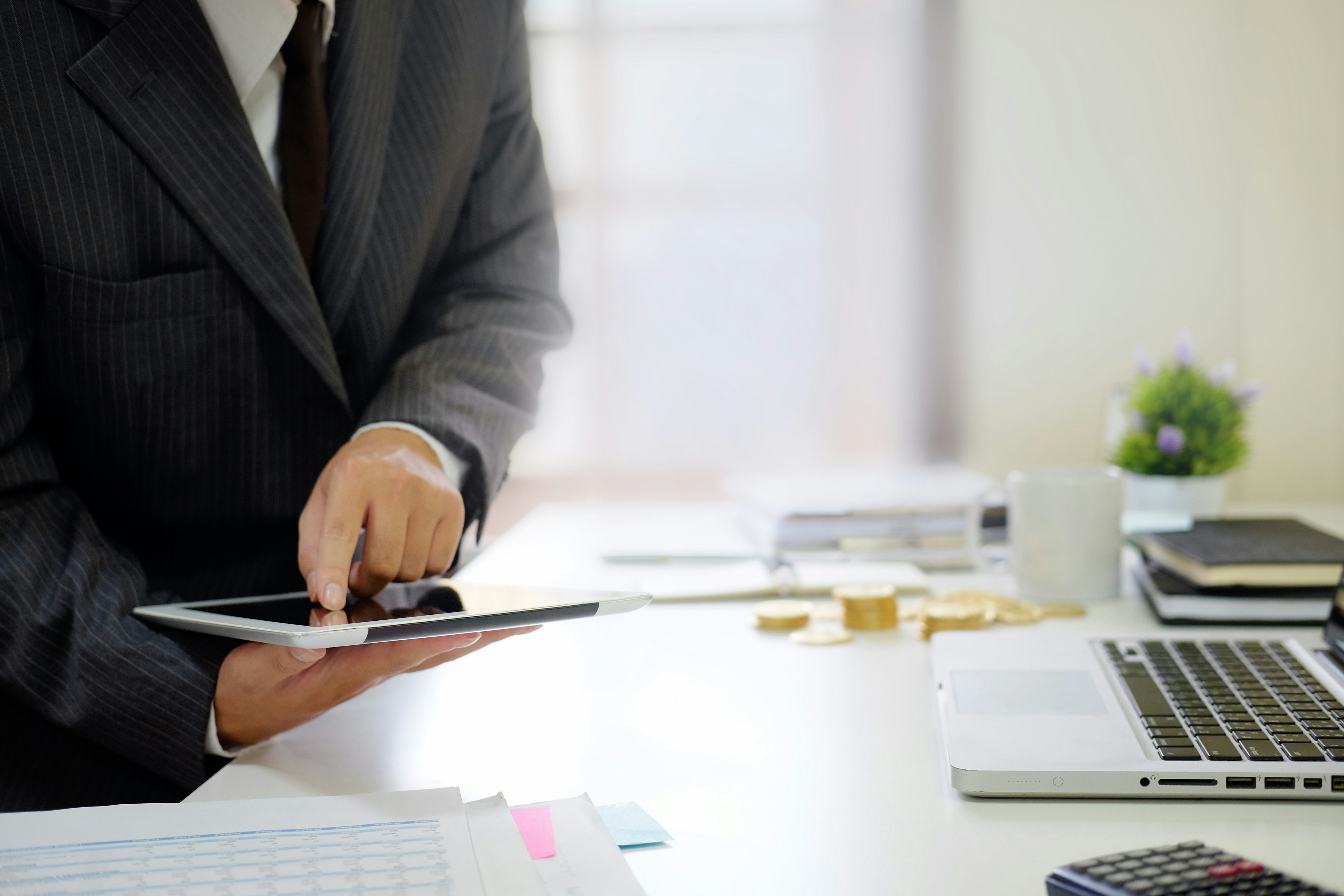 Business professional using a tablet at a desk with documents and a laptop